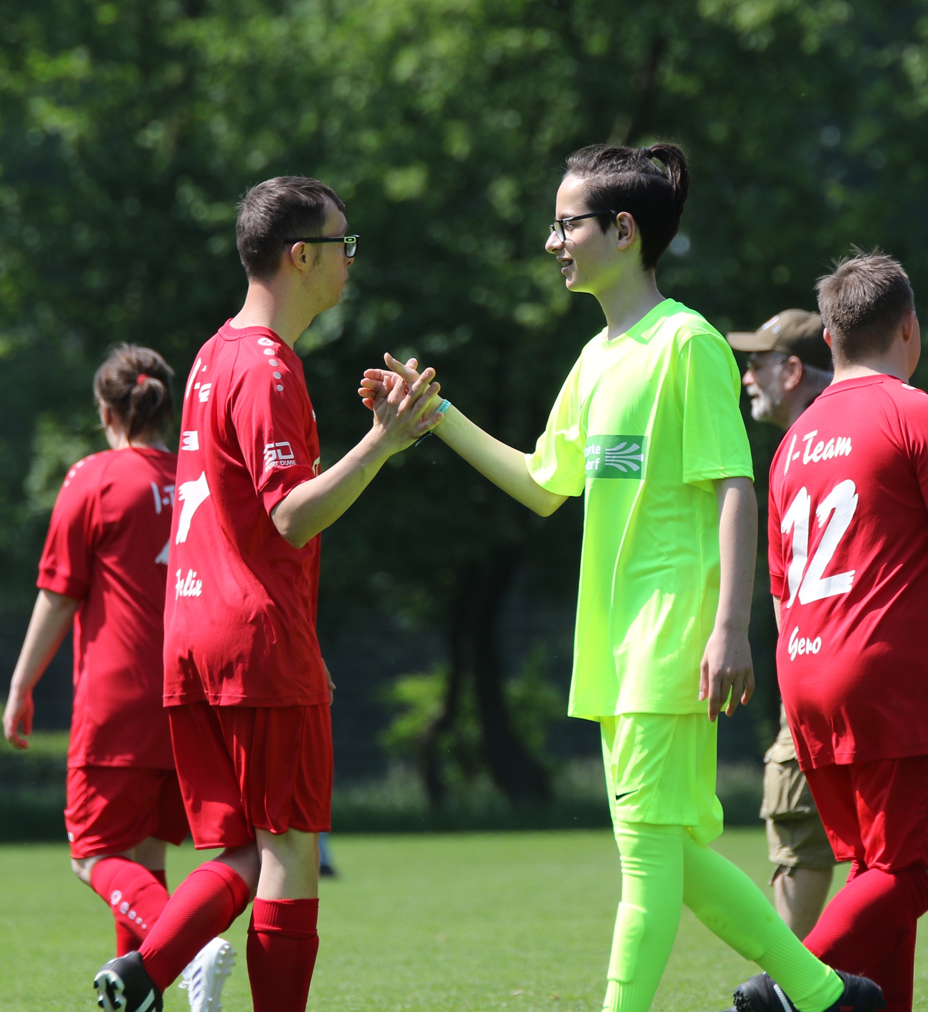 [{"clang_id":1,"value":"Fußballspiel: Zwei Spielerinnen/Spieler mit verschränkten Händen. Links rot, rechts neon-gelb gekleidet. Im Hintergrund weitere Fußballspieler. Grünfläche."}]