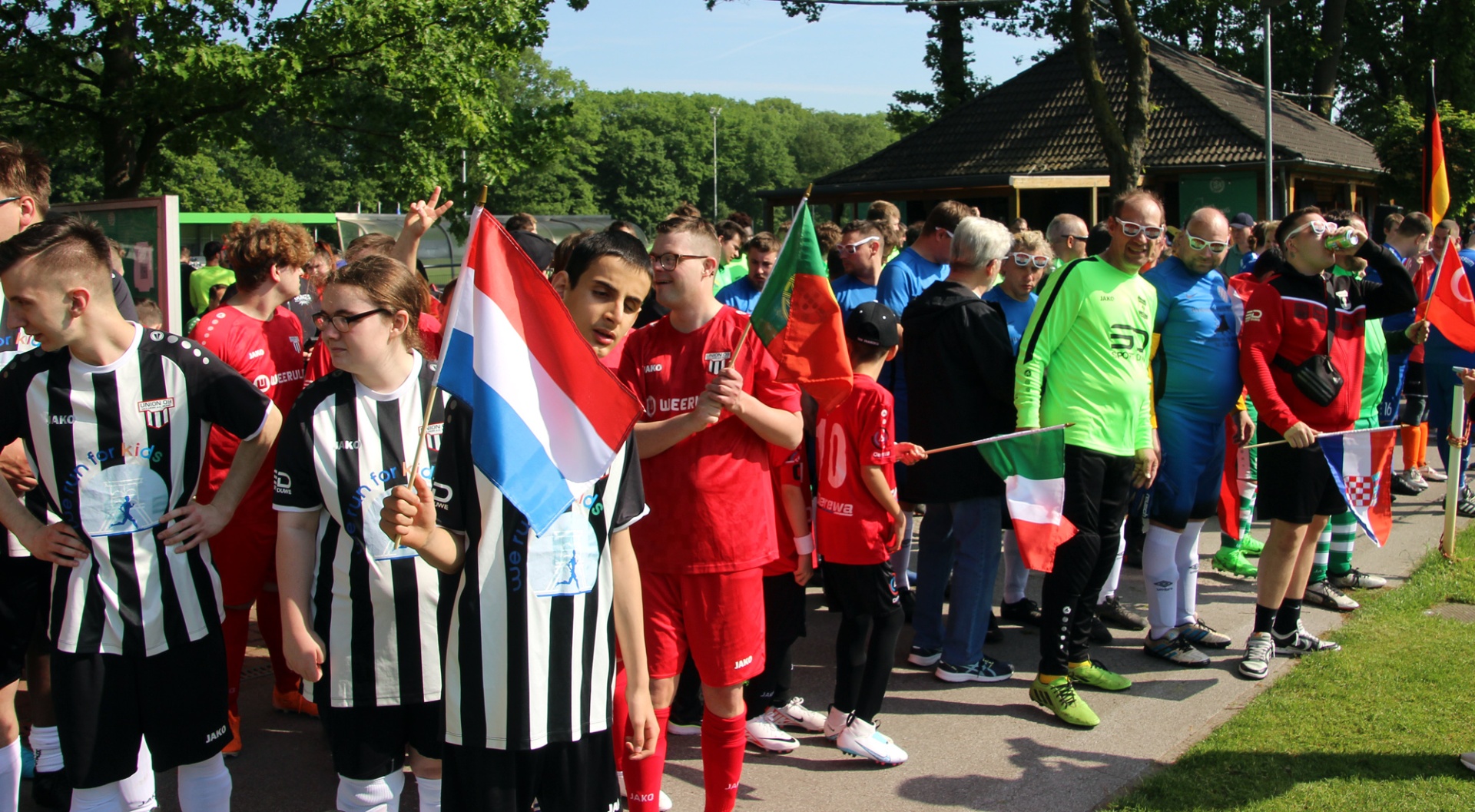 [{"clang_id":1,"value":"Jugendfußballturnier mit Spielern und Zuschauern. Mehrere Nationalflaggen (Niederlande, Kroatien, Italien, Deutschland) sind zu sehen."}]