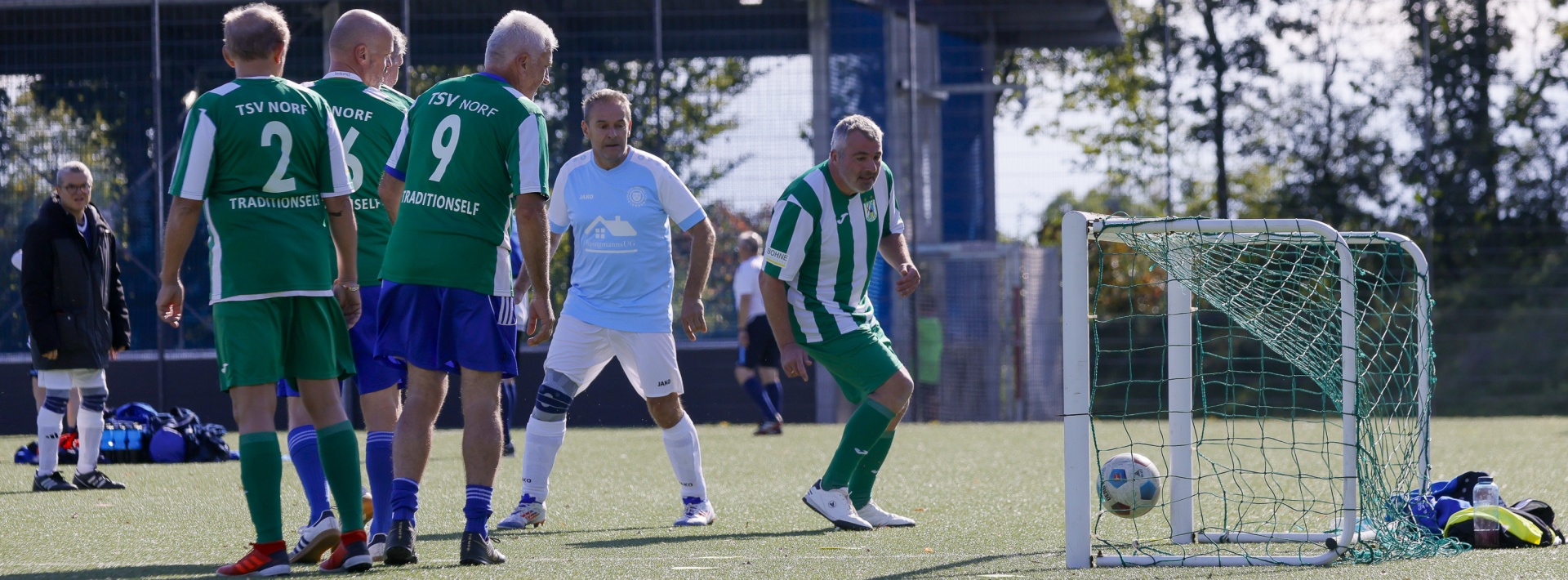[{"clang_id":1,"value":"Fußballspiel auf Rasenplatz. Vier Spieler stehen um einen Ball, zwei weitere im Hintergrund. Ein Tor mit Netz ist rechts zu sehen."}]