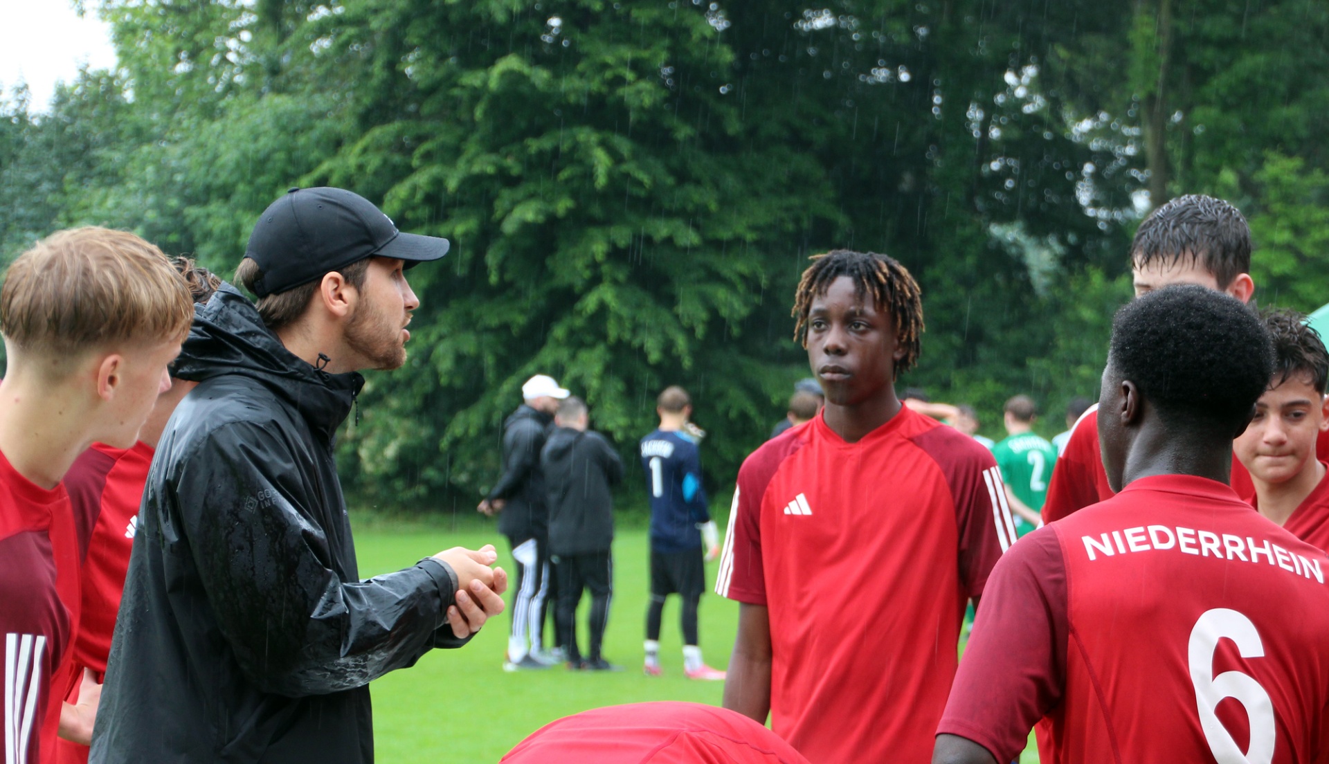 [{"clang_id":1,"value":"Fußballteam in roten Trikots und schwarzer Sportkleidung diskutiert auf grünem Rasen im Freien. Ein Trainer mit schwarzer Jacke und Kappe spricht mit den Spielern."}]