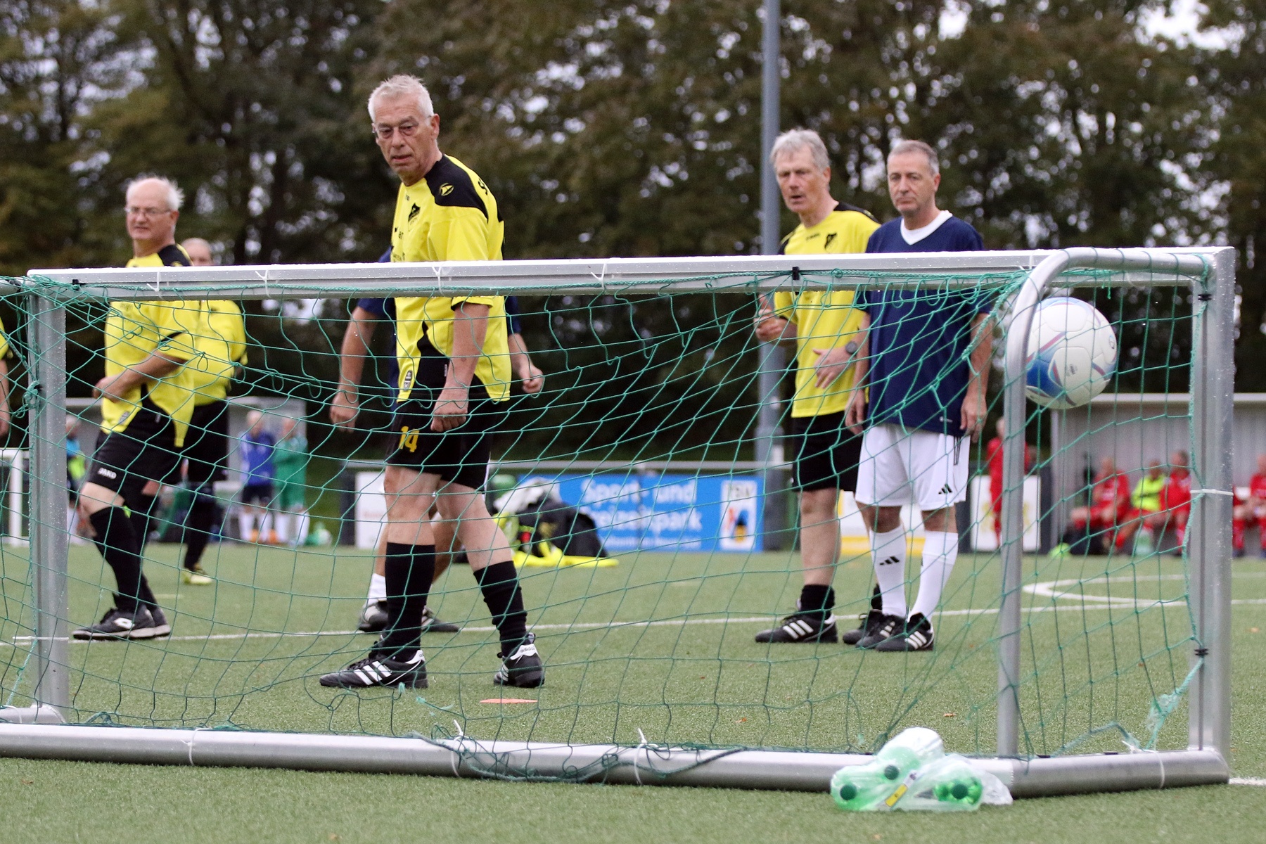 [{"clang_id":1,"value":"Fußballspieler mittleren Alters auf grünem Rasenfeld. Ein Spieler steht vor dem Tor, andere im Hintergrund. Alle tragen Sportkleidung."}]