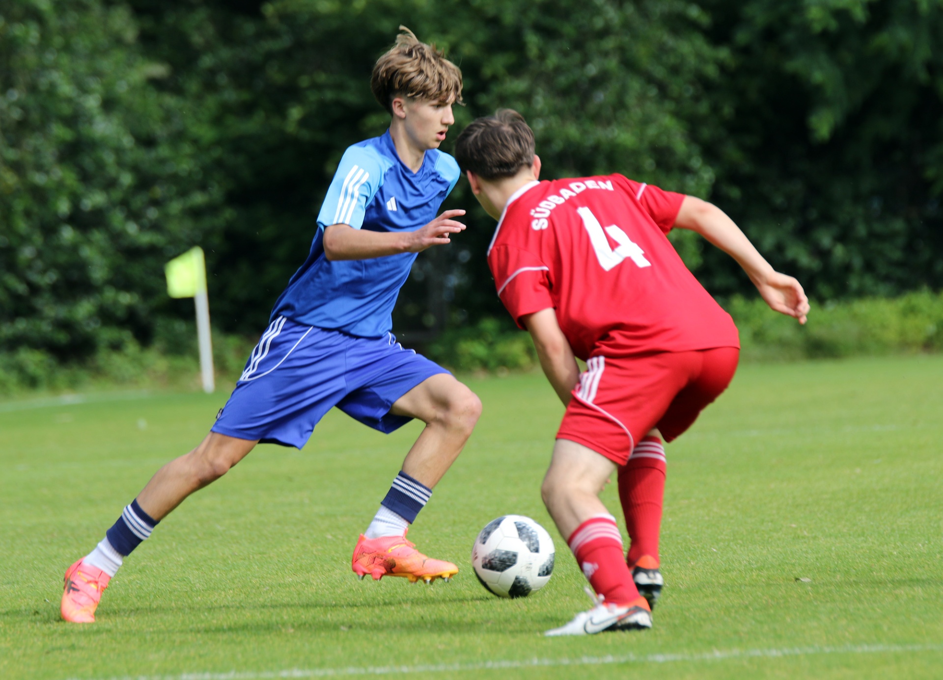 [{"clang_id":1,"value":"Zwei Fußballspieler auf einem Rasenfeld: Links ein Spieler in blauem Trikot, rechts in rotem Trikot mit Nummer 4, beide beim Dribbeln um den Ball."}]