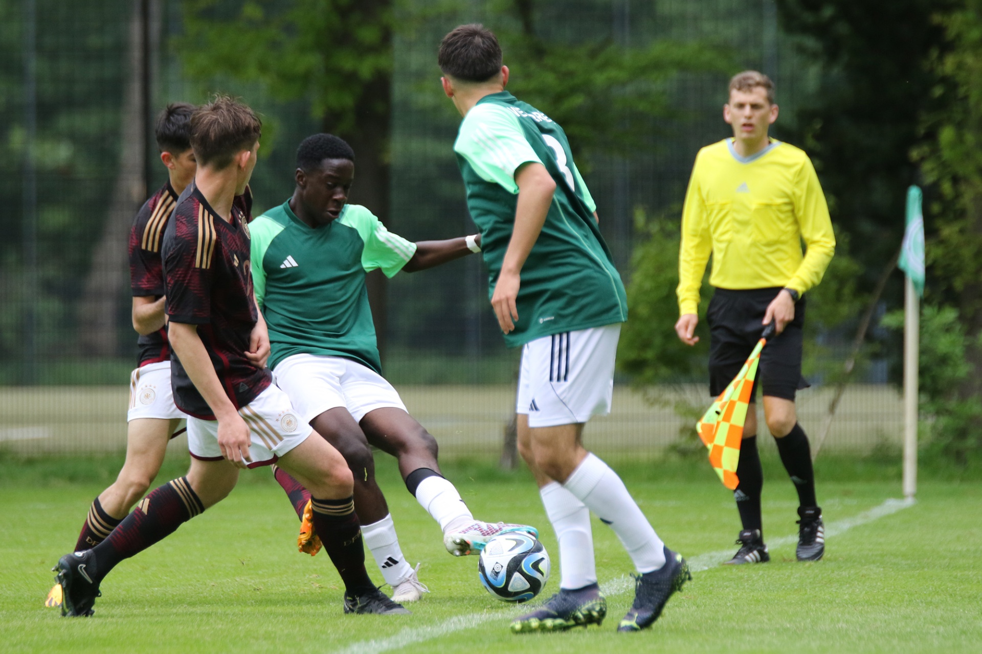 [{"clang_id":1,"value":"Fußballspiel: Zwei Spieler mit grünem Trikot kämpfen um den Ball. Im Hintergrund ein Spieler mit rotem Trikot und ein Schiedsrichter mit gelber Kleidung. Grasfläche."}]