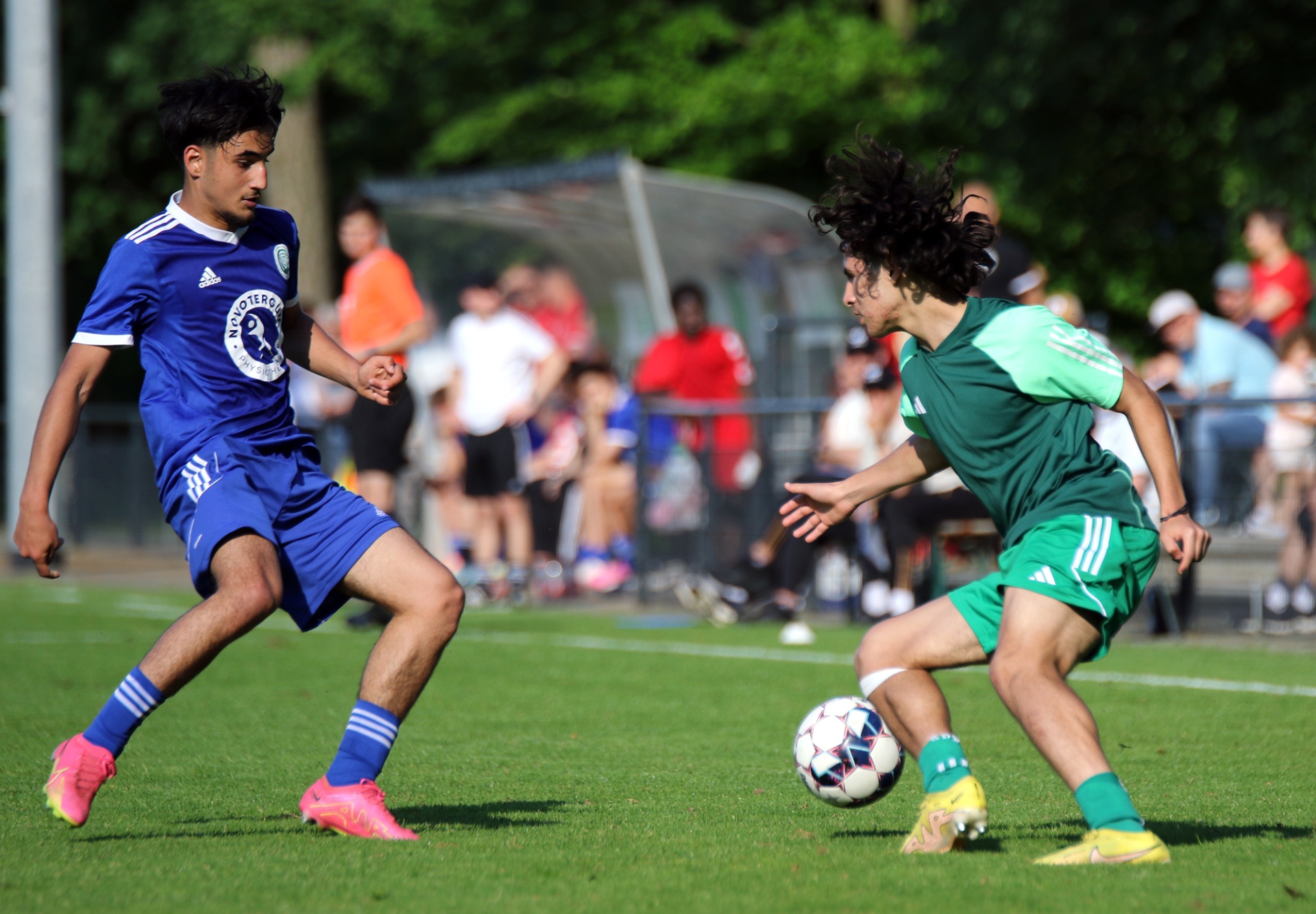 [{"clang_id":1,"value":"Zwei Fußballspieler im Wettkampf auf grünem Rasen. Links trägt ein Spieler blaues Trikot und pinke Schuhe, rechts ein Spieler grünes Trikot. Im Hintergrund Zuschauer."}]