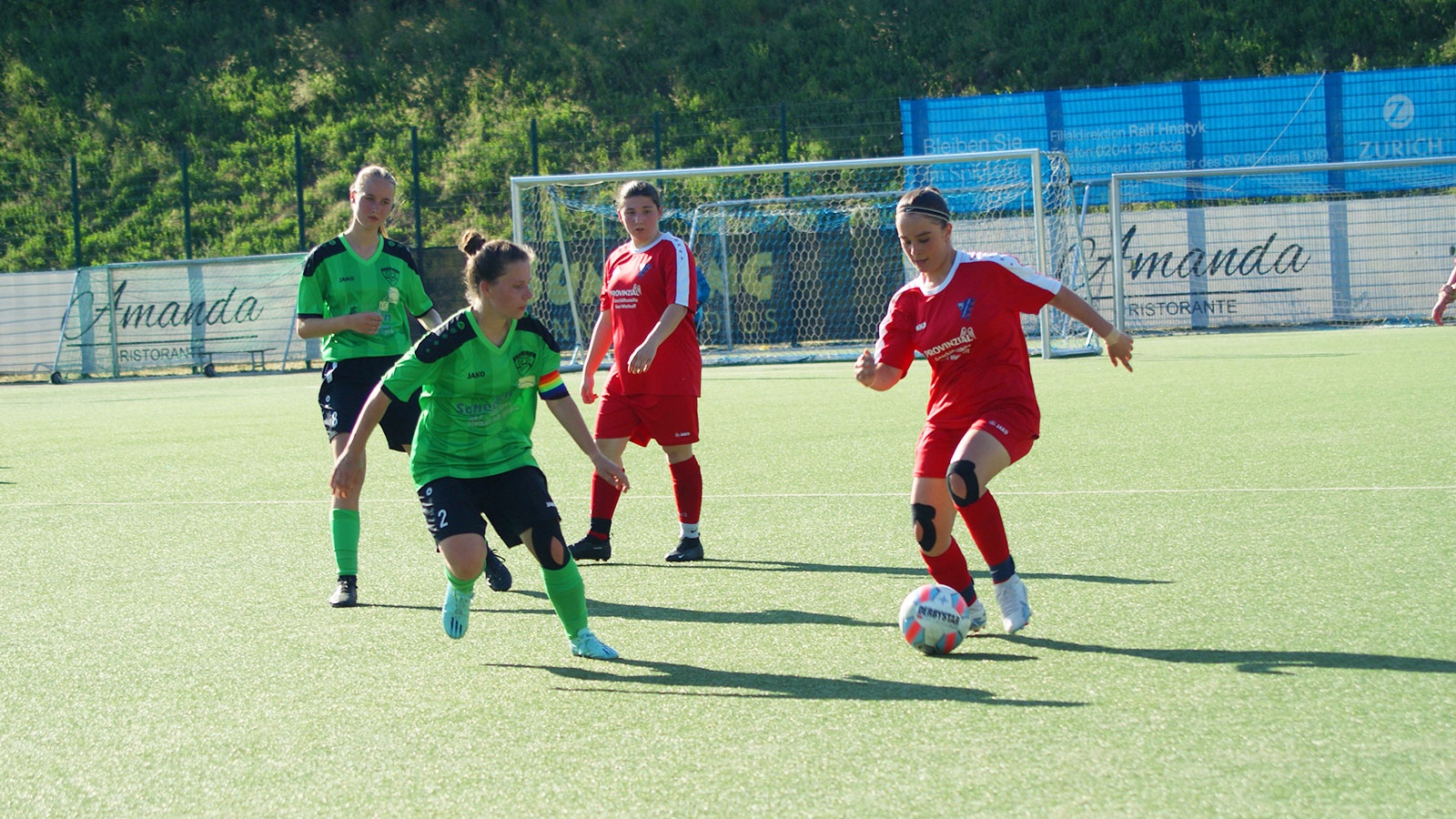 [{"clang_id":1,"value":"Fußballspiel: Drei Spielerinnen auf grünem Kunstrasen, eine dribbelt den Ball, die anderen stehen ihr gegenüber. Im Hintergrund Fußballtor und Bandenwerbung."}]