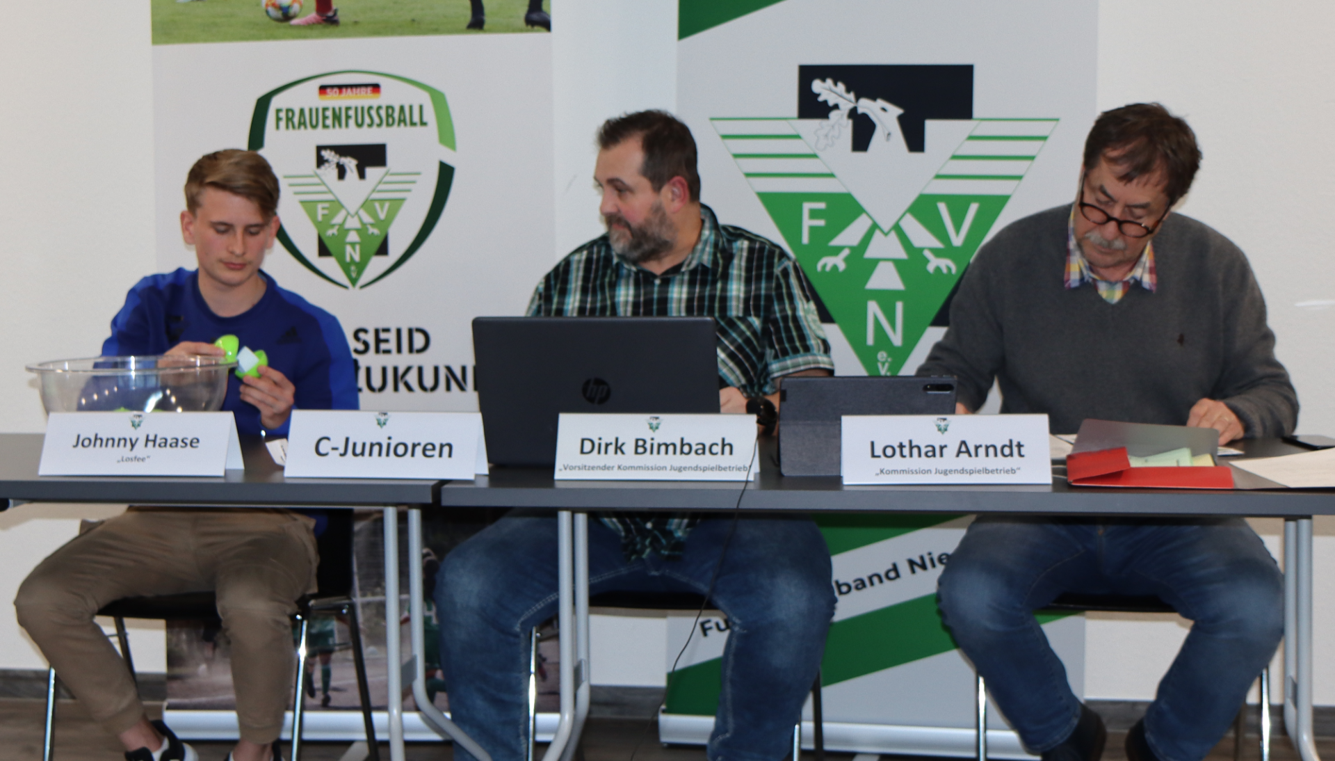 [{"clang_id":1,"value":"Vier Männer sitzen an einem Tisch vor einem Banner mit dem Logo \"FAV N\" und dem Schriftzug \"Frauenfußball\". Namensschilder identifizieren Johnny Haase, Dirk Bimbach und Lothar Arndt. Ein Laptop steht auf dem Tisch."}]