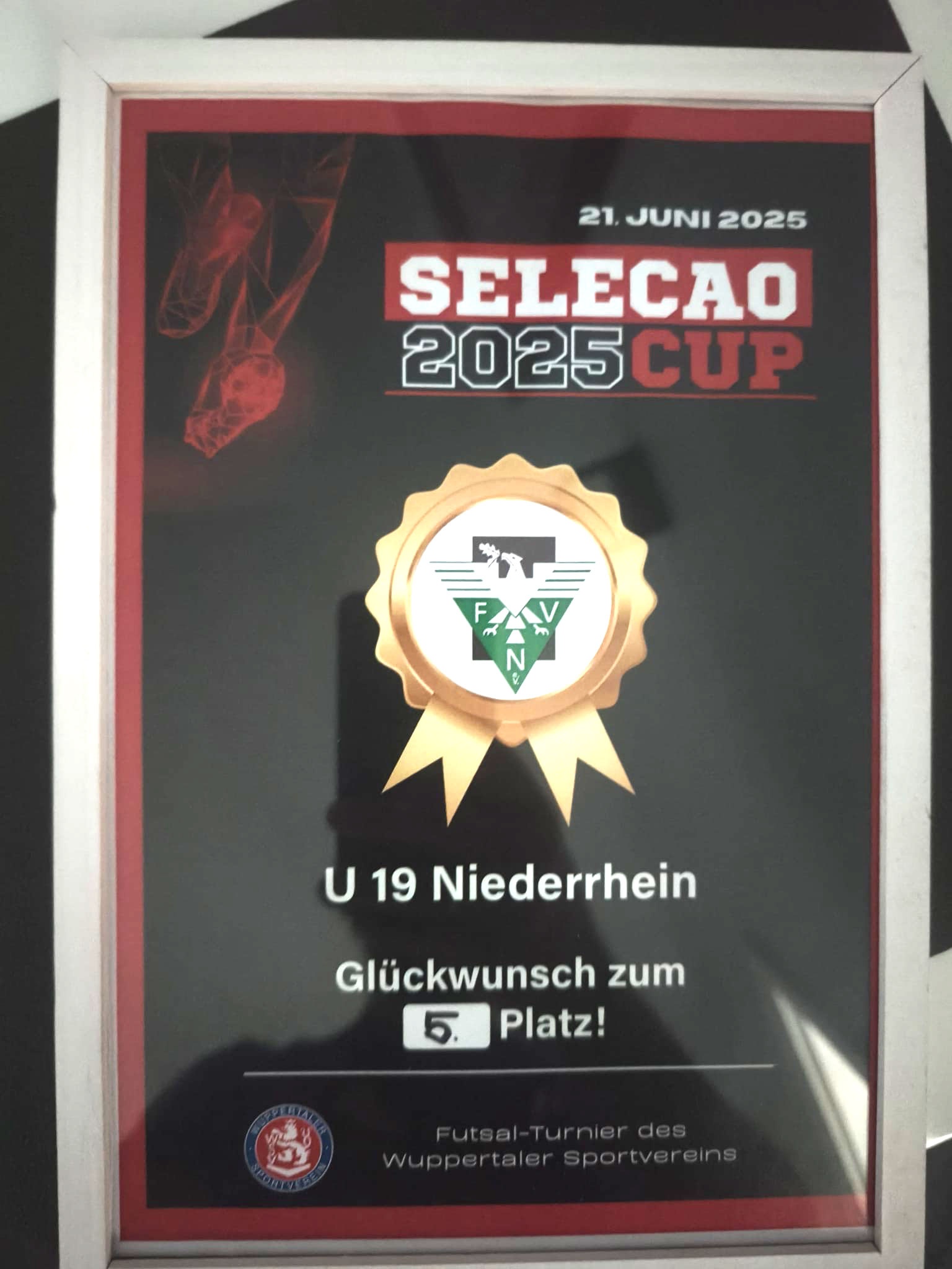 [{"clang_id":1,"value":"Pokal mit Aufschrift \"Selecao 2025 Cup\". Darunter \"U 19 Niederrhein\", \"Glückwunsch zum 5. Platz!\" und Logo des Wuppertaler Sportvereins. Dunkler Hintergrund."}]