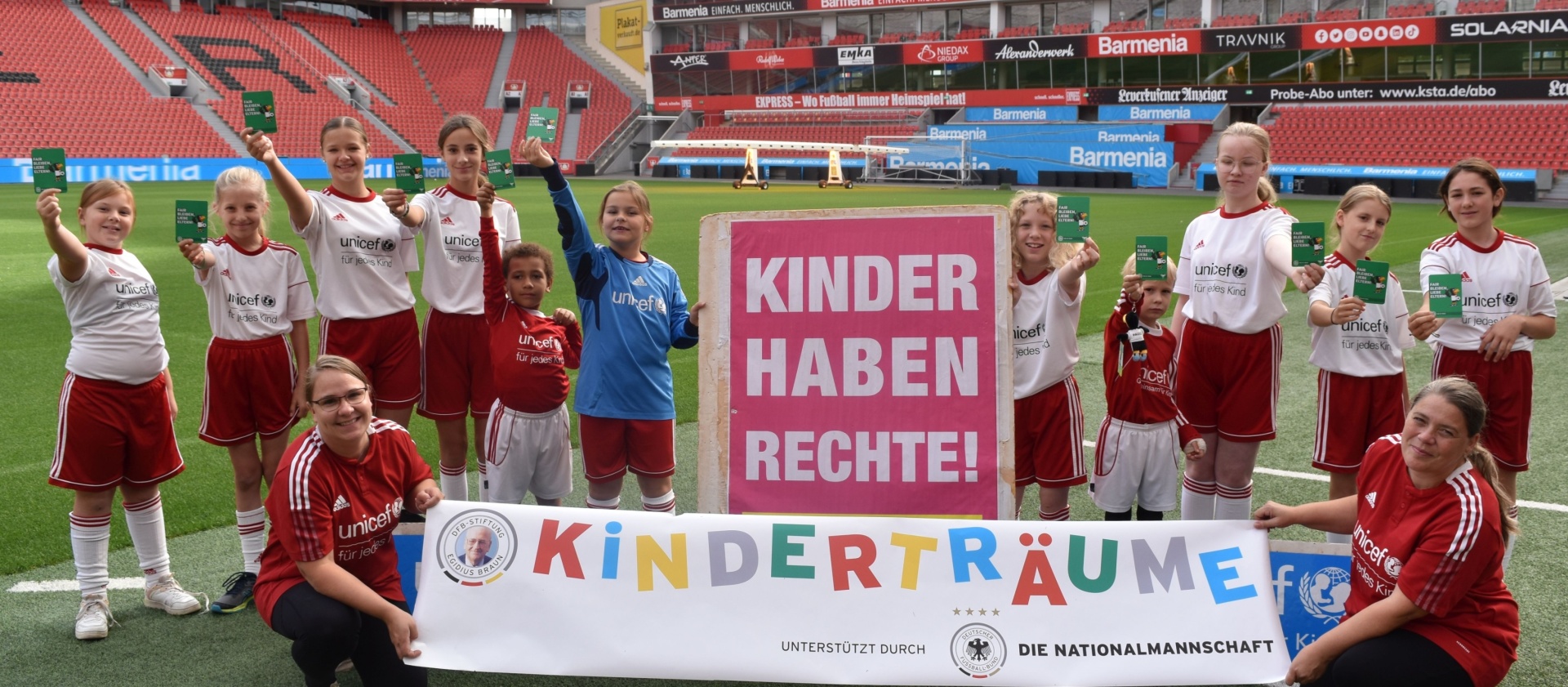 [{"clang_id":1,"value":"Fußballmannschaft mit Banner \"Kinder haben Rechte! Kinderträume\" im Stadion. Spieler tragen rote und weiße Trikots. UNICEF-Logo sichtbar."}]