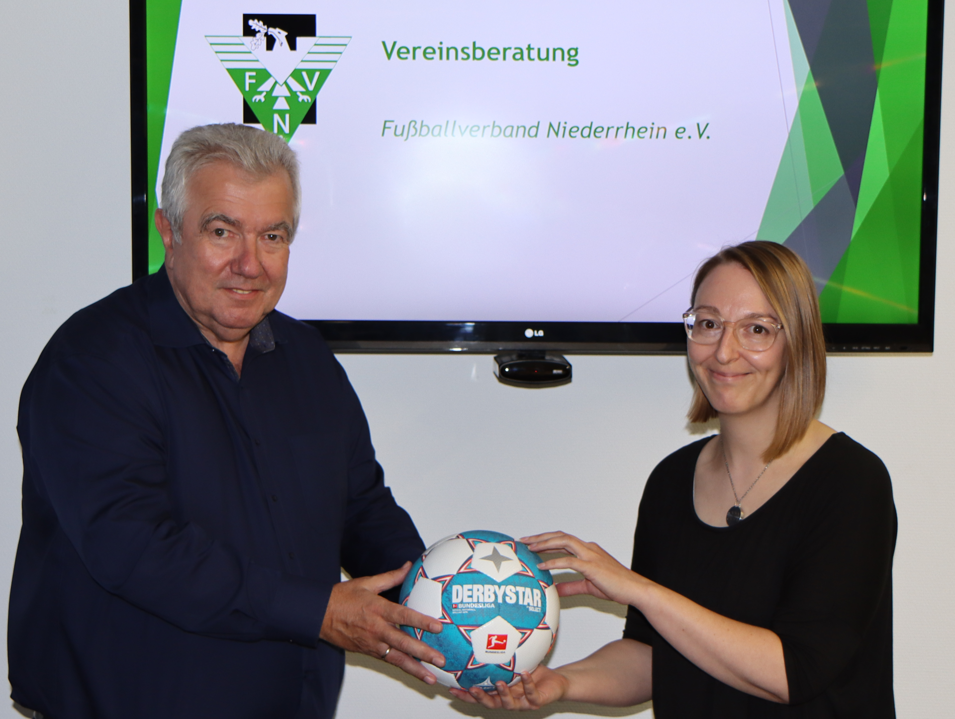 [{"clang_id":1,"value":"Zwei Personen halten einen Fußball vor sich. Im Hintergrund eine Präsentation mit Logo und Schriftzug \"Fußballverband Niederrhein e.V.\"."}]