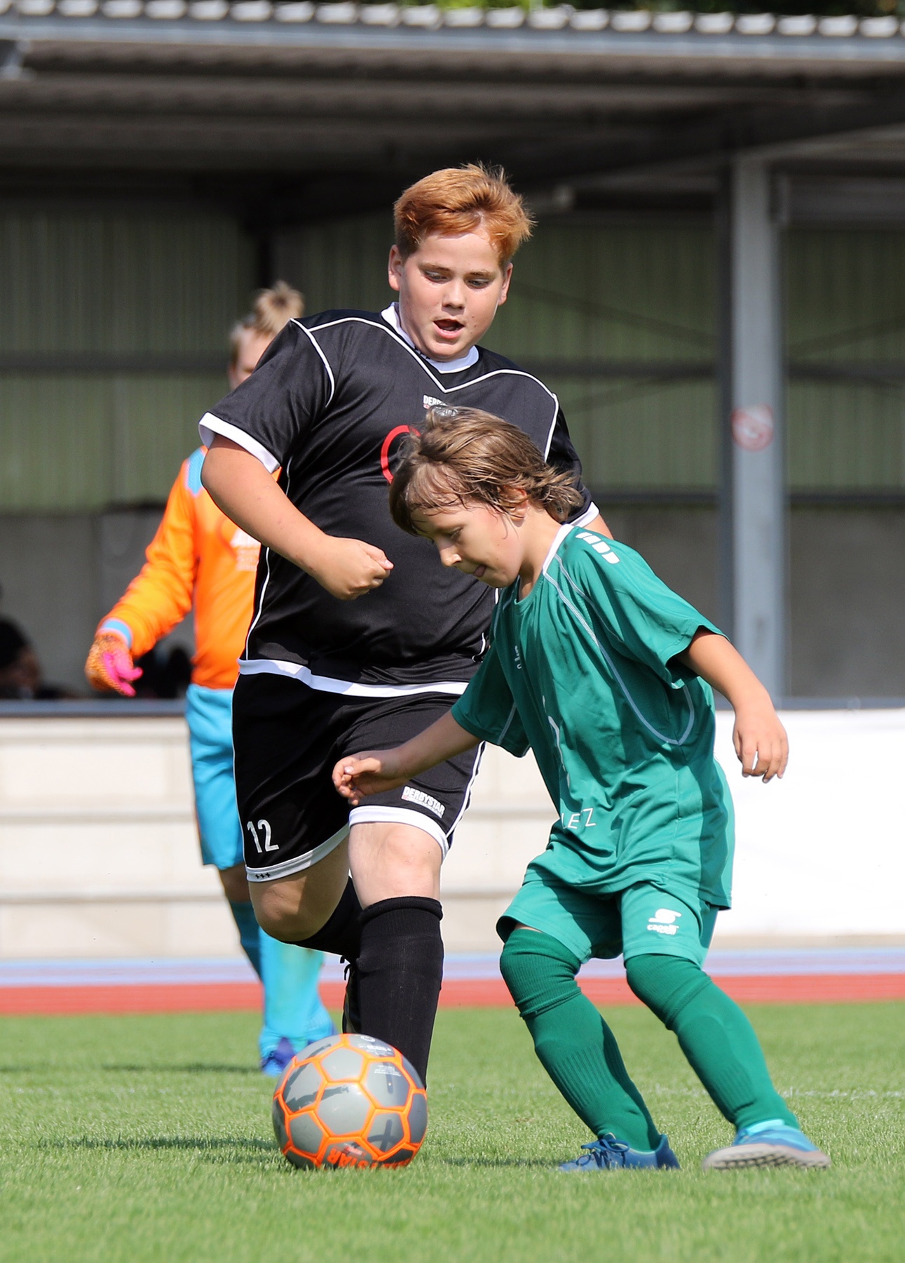 [{"clang_id":1,"value":"Zwei Fussballspieler, ein rothaariger mit schwarzem Trikot und ein dunkelhaariger in grün, kämpfen um den Ball auf einem Rasenplatz. Im Hintergrund Zuschauer."}]
