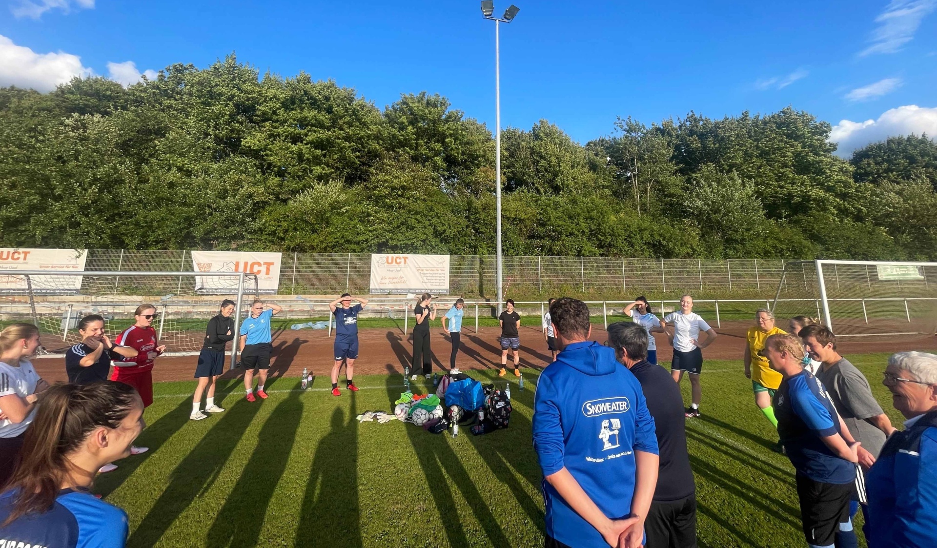 [{"clang_id":1,"value":"Fußballfeld mit Spielern in Trainingskleidung. Im Hintergrund Bäume und eine Reklametafel. Eine Person mit blauem Shirt steht mit dem Rücken zum Betrachter."}]