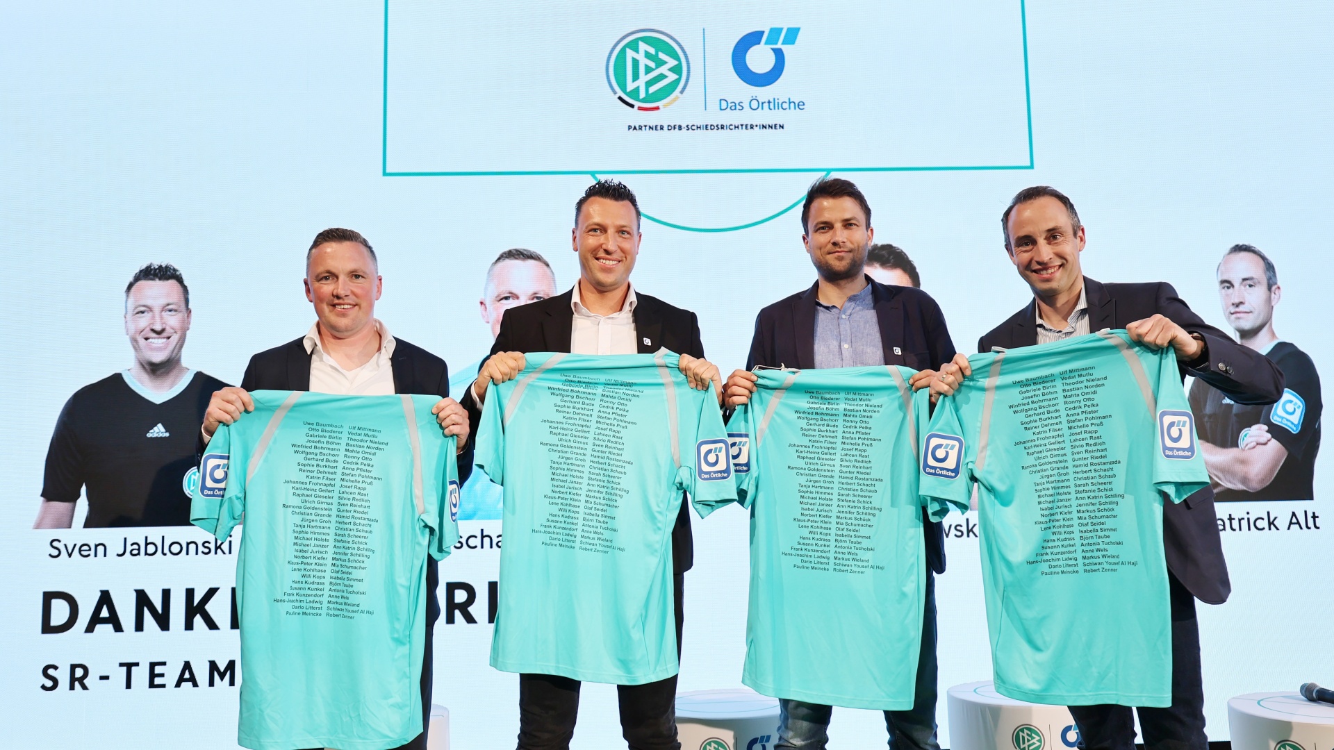 [{"clang_id":1,"value":"Gruppe von Männern präsentiert grüne Fußballtrikots mit Werbelogo vor hellem Hintergrund. Links und rechts Namen und Schriftzüge."}]