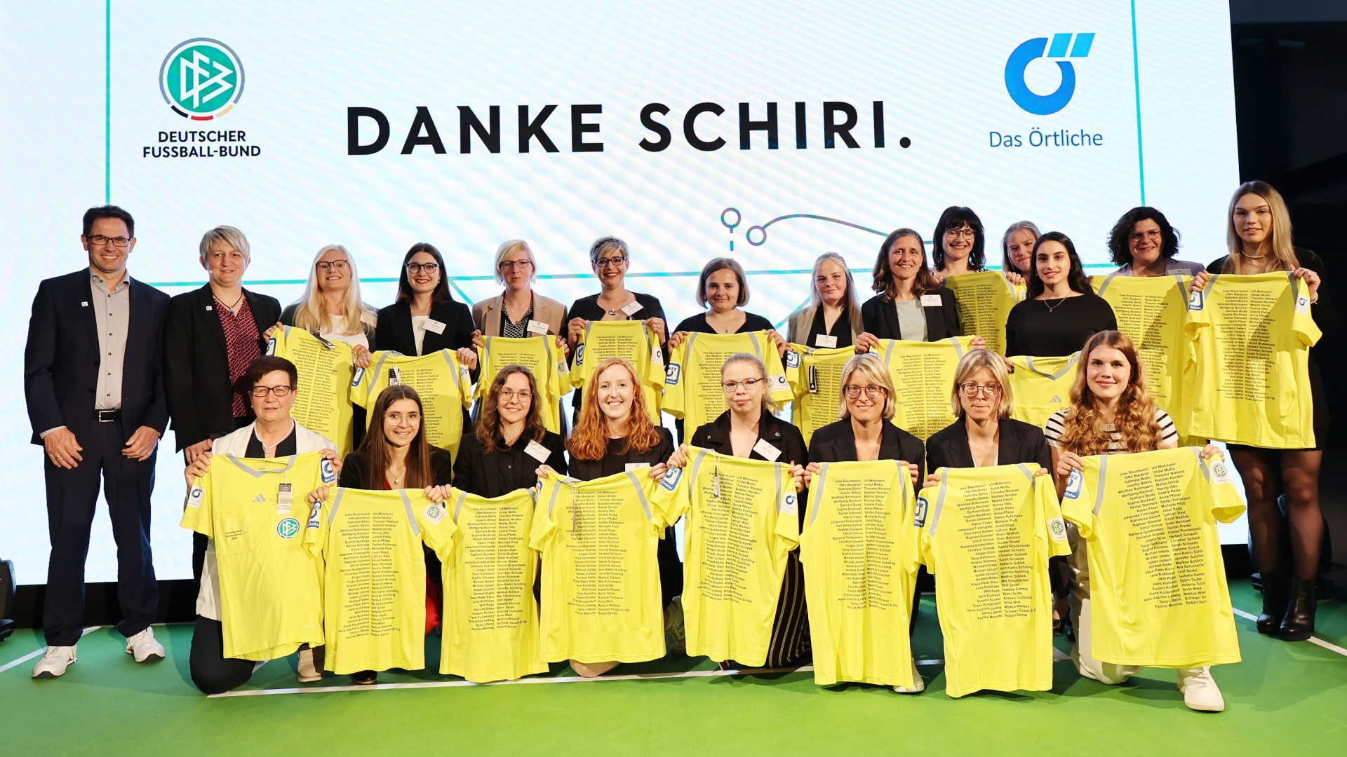 [{"clang_id":1,"value":"Gruppe von etwa 20 Personen vor einer hellen Wand mit dem Schriftzug \"DANKE SCHIRI.\". Sie halten gelbe Trikots mit Texten in den Händen."}]