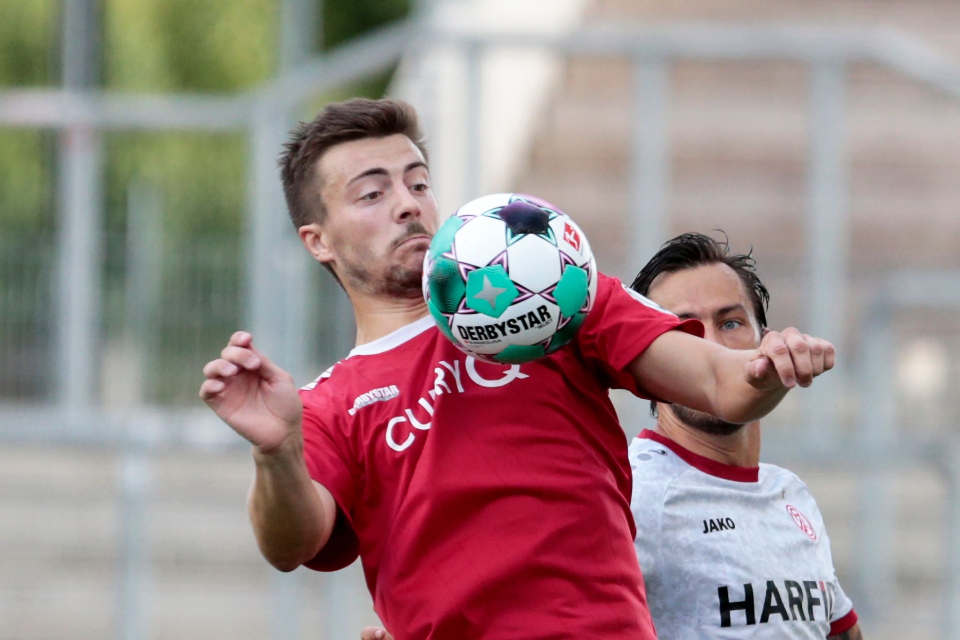 [{"clang_id":1,"value":"Zwei Fußballspieler kämpfen um einen Ball. Ein Spieler in rotem Trikot mit \"CURRY\" Aufdruck köpft den Ball, dahinter ein Spieler in grau-rotem Trikot mit \"HARF\" Aufdruck."}]