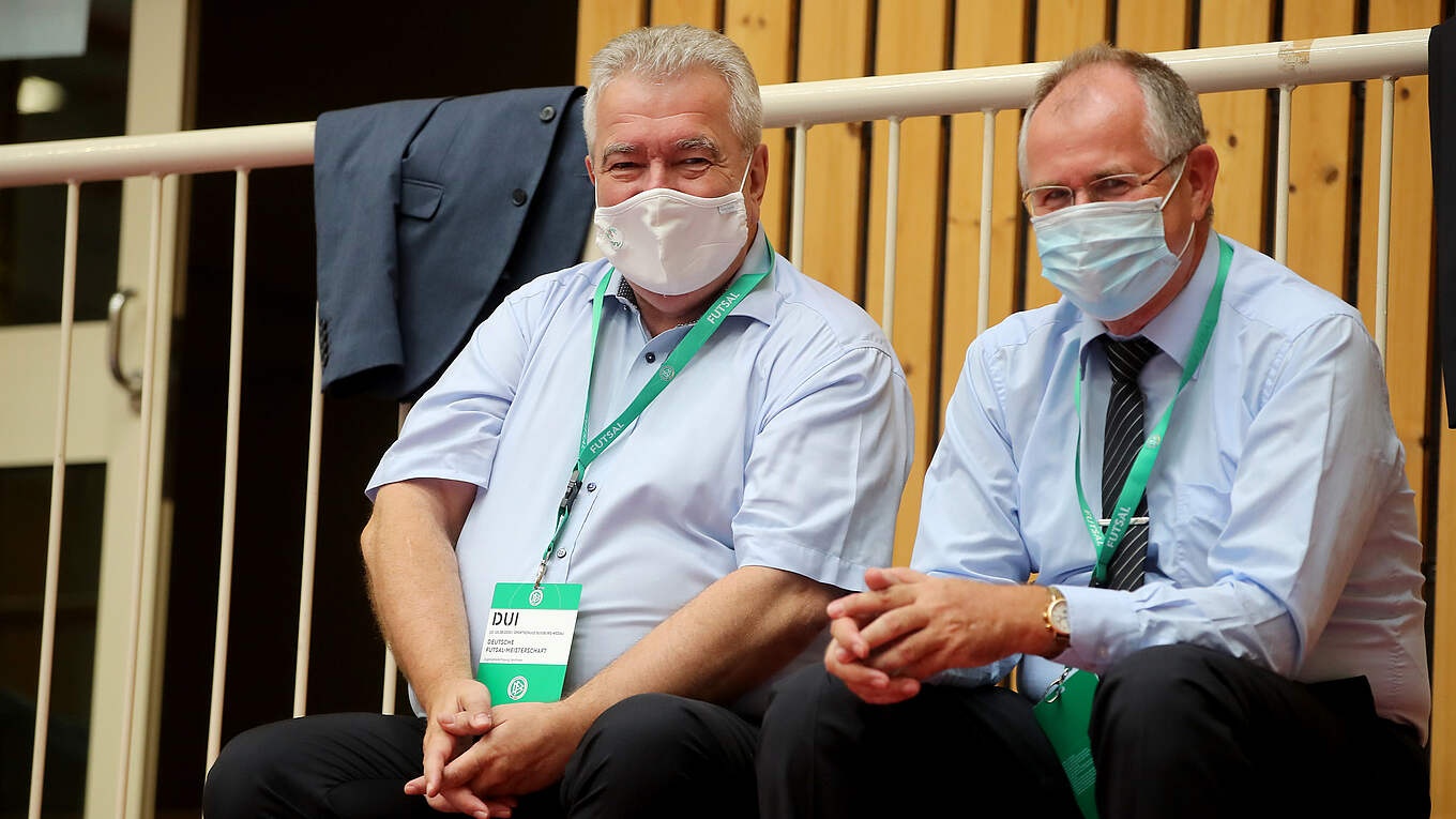 [{"clang_id":1,"value":"Zwei ältere Männer mit Hemd und Krawatte sitzen nebeneinander, beide tragen medizinische Masken und Namensschilder mit der Aufschrift \"DUI\". Im Hintergrund eine Holzvertäfelung."}]
