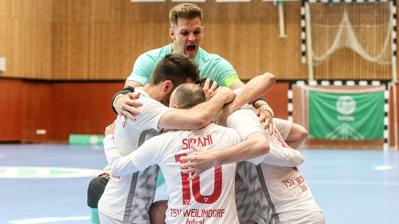 [{"clang_id":1,"value":"Futsal-Spieler feiern einen Treffer. Vier Sportler in weißen und roten Trikots umarmen sich jubelnd, ein fünfter steht hinter ihnen und schreit. Hallenfußballfeld im Hintergrund."}]