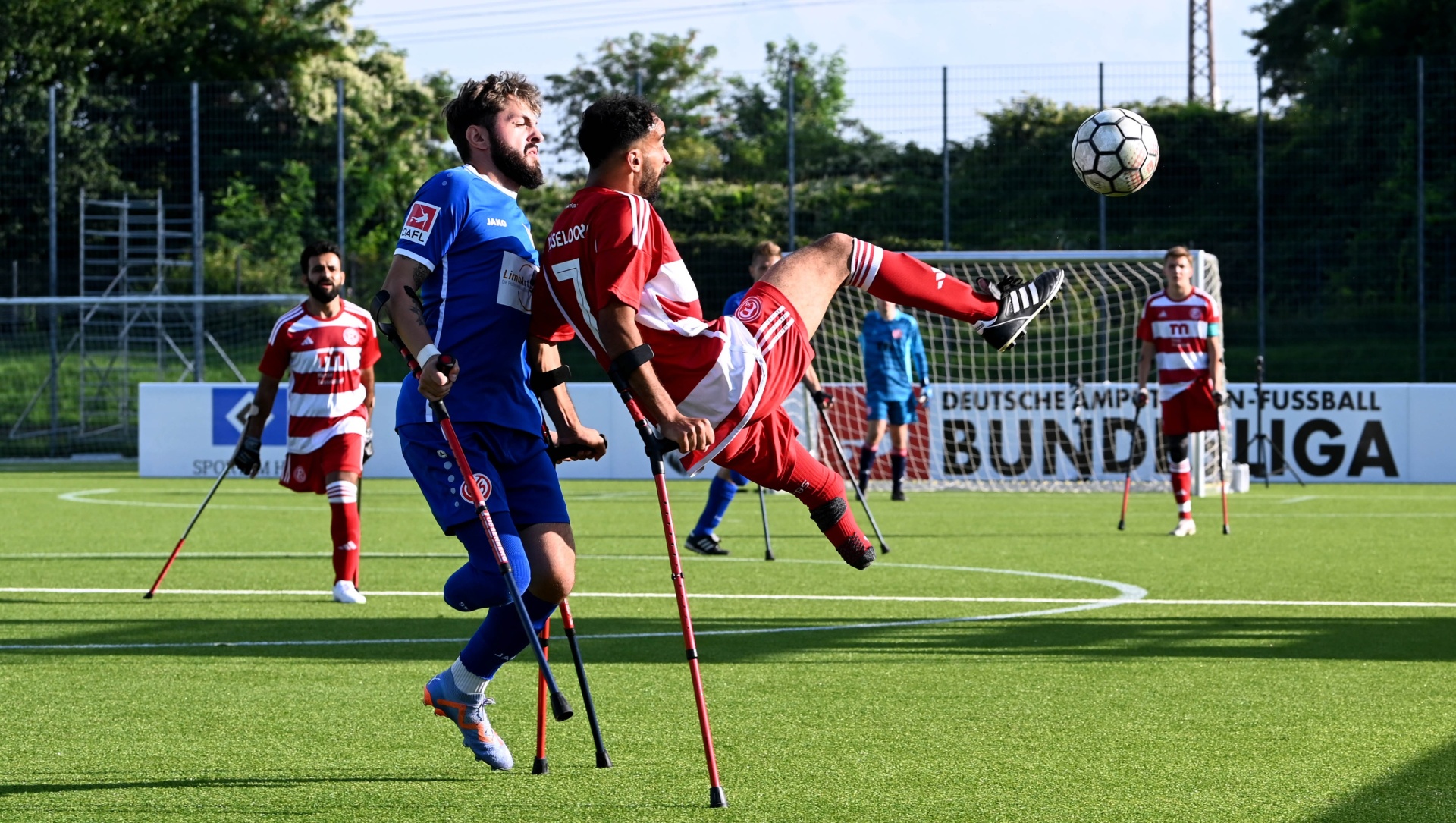 [{"clang_id":1,"value":"Zwei Fußballspieler mit Gehkrücken springen nacheinander, um einen Ball auf einem grünen Fußballfeld zu köpfen. Im Hintergrund eine Zuschauertribüne."}]