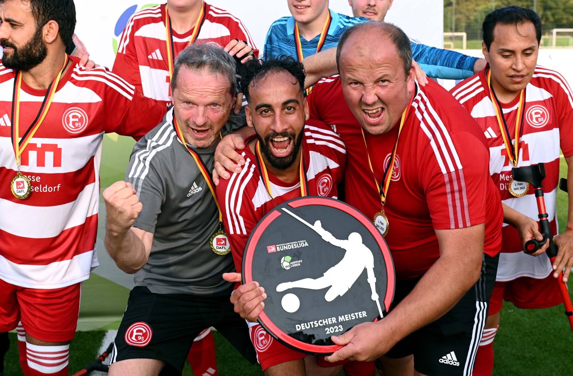 [{"clang_id":1,"value":"Fußballteam mit Pokal \"Deutscher Meister 2023\". Sie tragen rote und weiße Trikots und freuen sich. Im Hintergrund weitere Spieler auf dem Rasen."}]