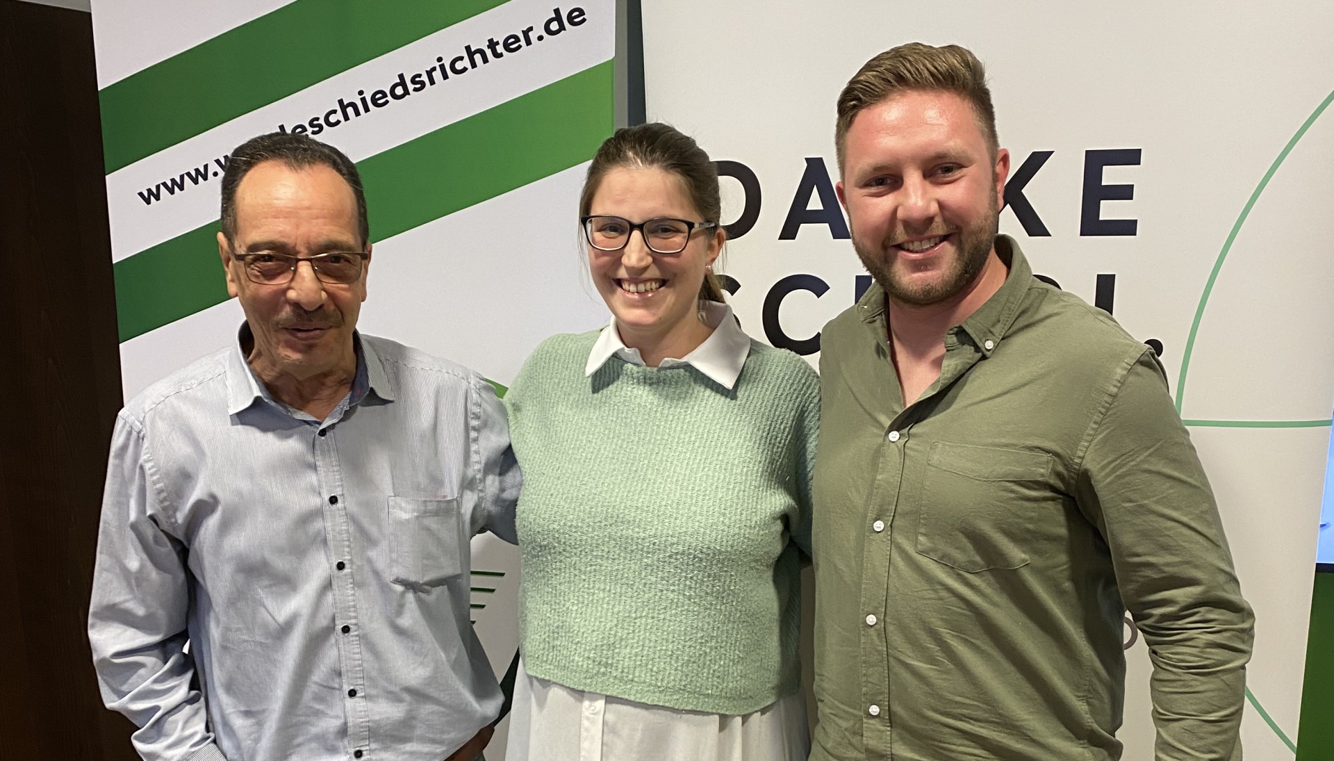 [{"clang_id":1,"value":"Drei Personen vor Hintergrund mit Schriftzug \"DANKE\". Links älterer Mann mit Brille, Mitte junge Frau mit Brille, rechts Mann mit Bart."}]
