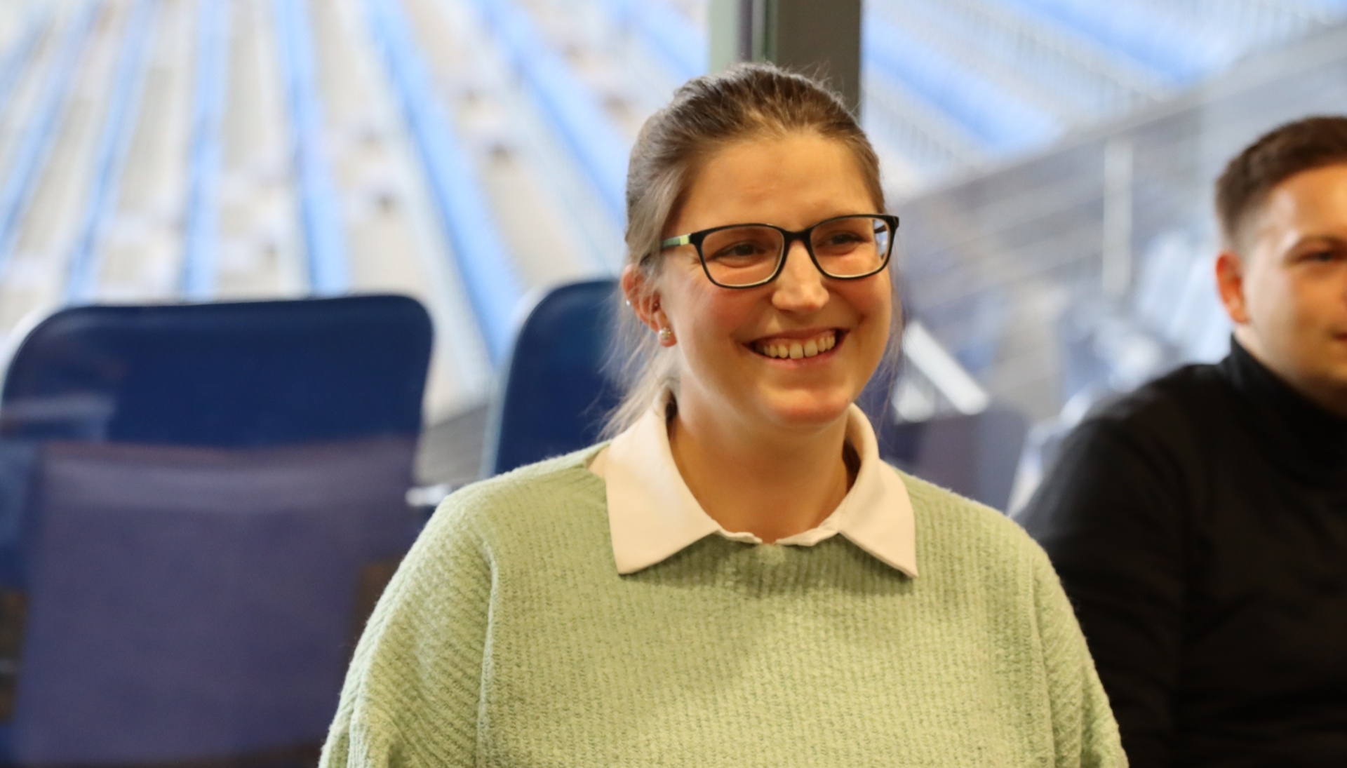 [{"clang_id":1,"value":"Frau mit Brille lächelt in einem Zug. Sie trägt einen hellgrünen Pullover mit weißem Kragen. Im Hintergrund sind blaue Sitze und ein Fenster zu sehen."}]