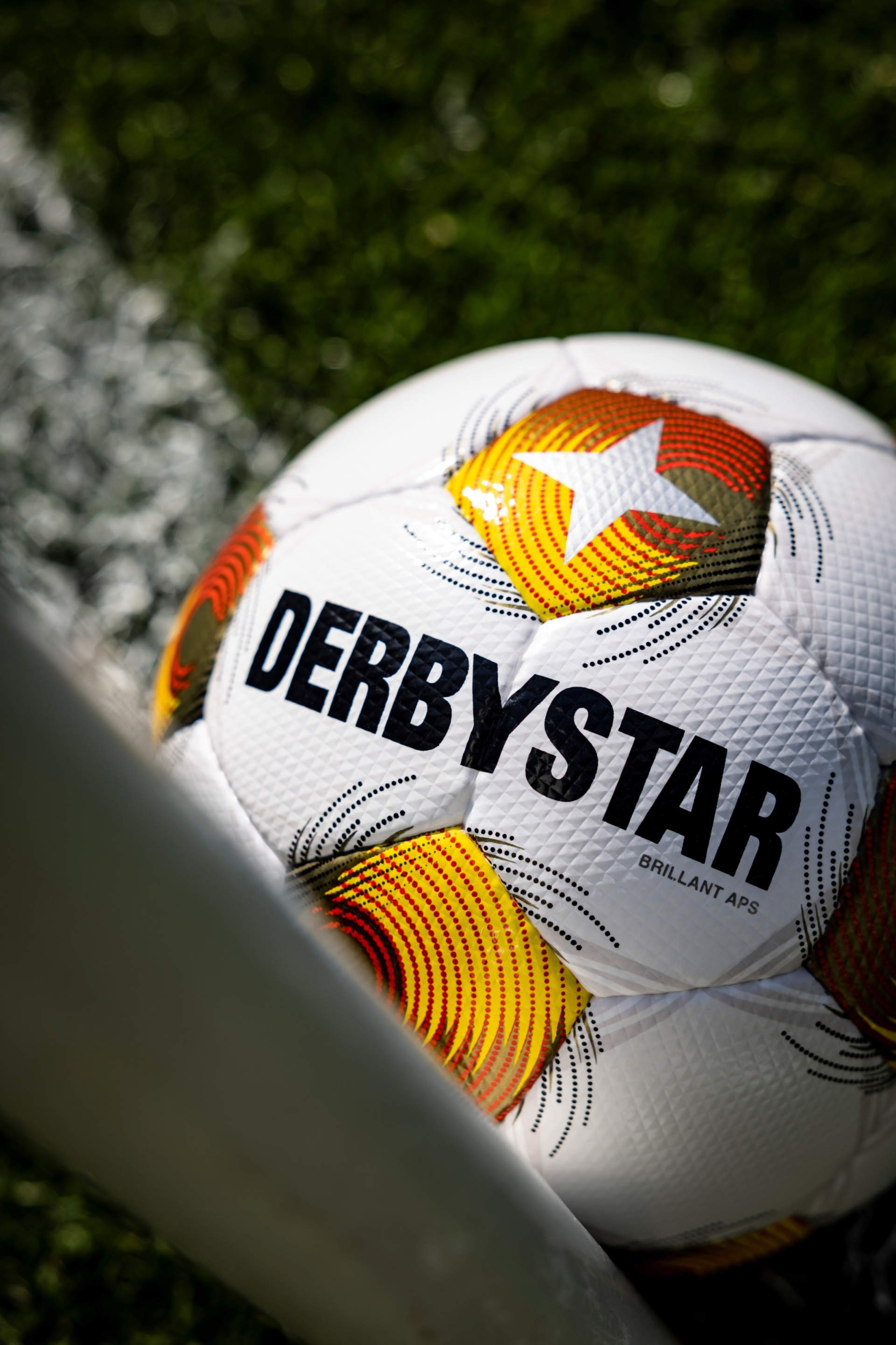 [{"clang_id":1,"value":"Fußball \"Derbystar\" mit orangefarbenen und schwarzen Akzenten liegt auf Gras. Ein Fuß ist im Bild zu sehen."}]