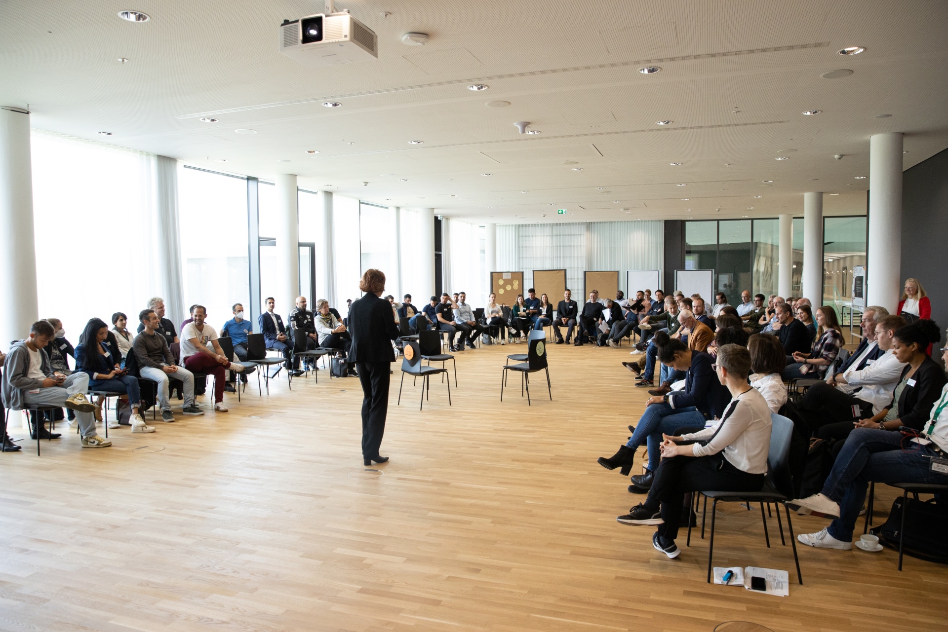 [{"clang_id":1,"value":"Großer Raum mit rund 50 Personen, die einem Mann in Anzug zuwenden. Alle sitzen auf Stühlen in einem Kreis. Helles Holzparkett, Fenster an der Seite."}]