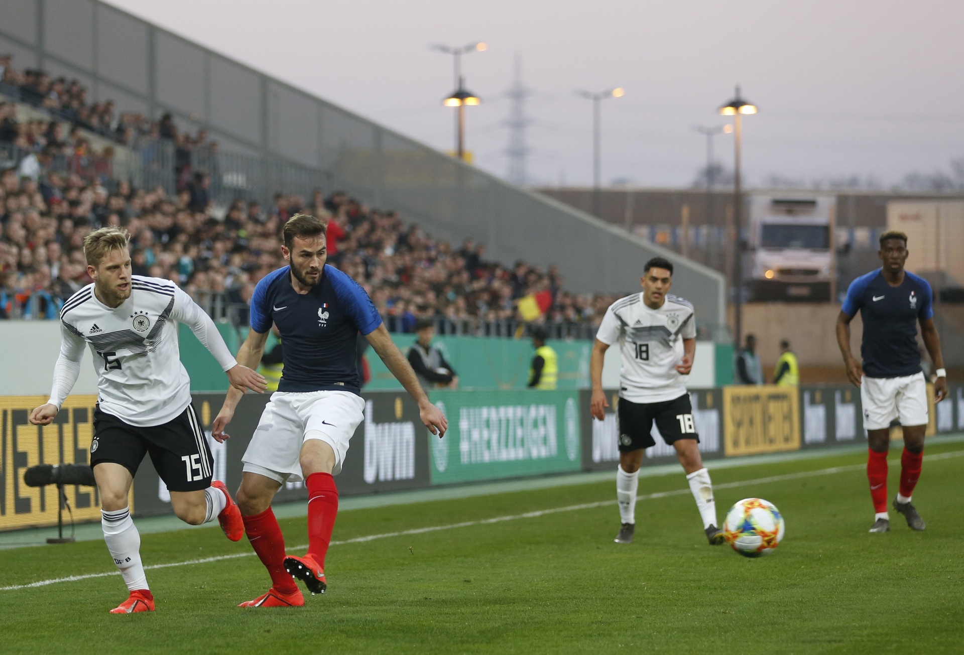 [{"clang_id":1,"value":"Fußballspiel Deutschland gegen Frankreich. Zwei Spieler dribbeln den Ball, weitere stehen in der Nähe. Zuschauerreihen im Hintergrund."}]