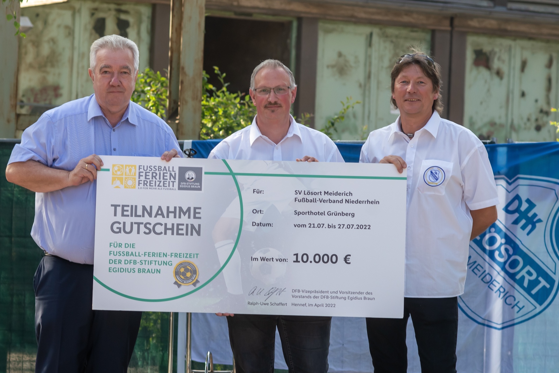 [{"clang_id":1,"value":"Vier Männer halten einen großen Scheck mit dem Wert 10.000 Euro vor einem Gebäude. Der Scheck ist für eine Fußball-Ferienfreizeit des SV Lösort Meiderich."}]
