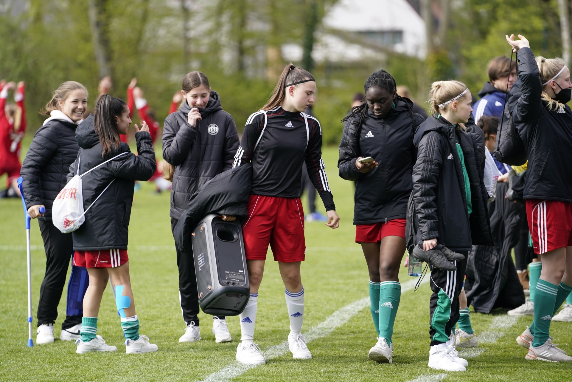 [{"clang_id":1,"value":"Fußballspielerinnen auf Rasenfeld. Einige tragen Trainingsanzüge, andere Sportkleidung. Eine Gruppe geht mit einem tragbaren Lautsprecher."}]
