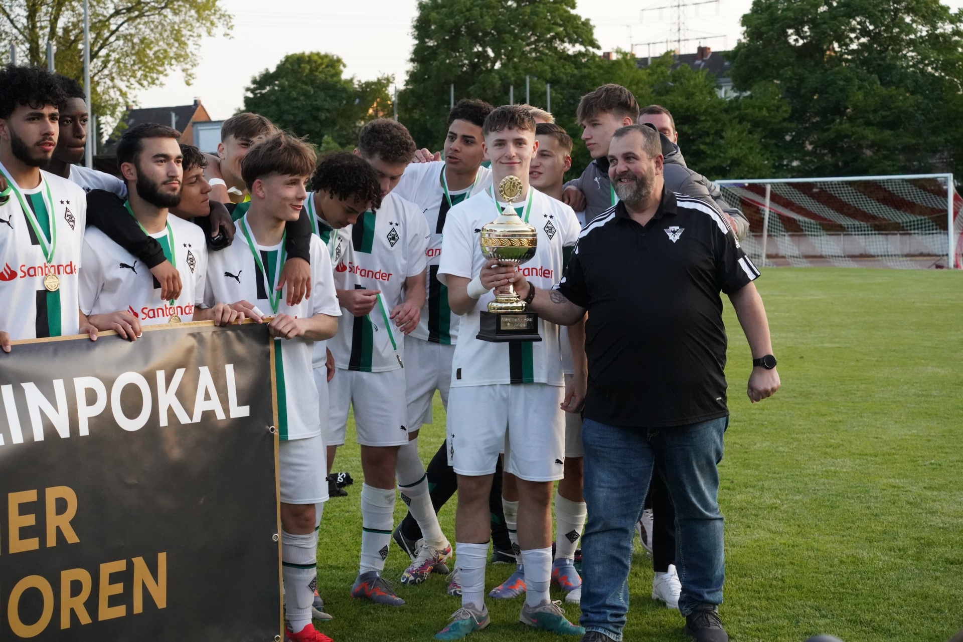 [{"clang_id":1,"value":"Fußballmannschaft in grünen Trikots mit Pokal und Trainer. Im Hintergrund ein Fußballfeld und ein Banner mit Schriftzügen."}]