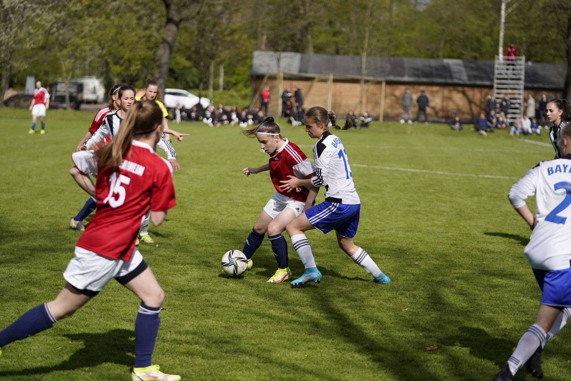 [{"clang_id":1,"value":"Fußballspiel: Zwei Spielerinnen in Rot und Blau kämpfen um den Ball auf einem grünen Rasenfeld. Im Hintergrund weitere Spieler und Zuschauer."}]
