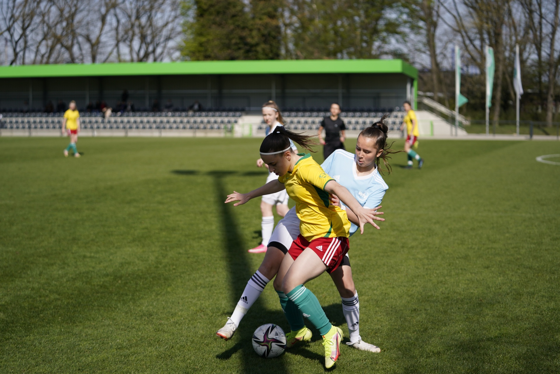[{"clang_id":1,"value":"Zwei Fußballspielerinnen kämpfen um den Ball auf einem grünen Rasenplatz. Im Hintergrund weitere Spielerinnen und ein Sportstadion."}]