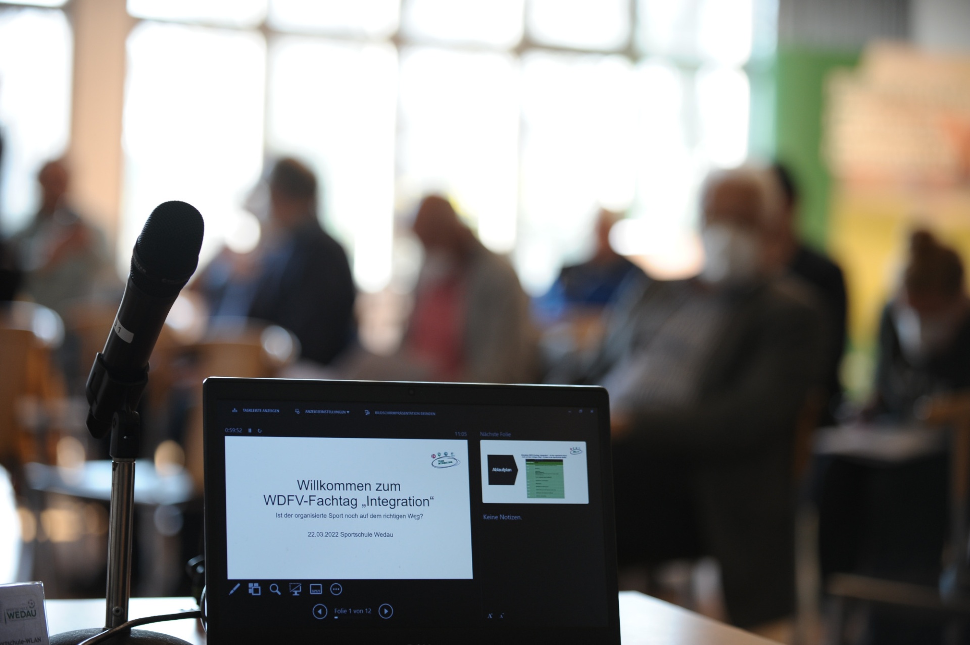 [{"clang_id":1,"value":"Konferenzraum. Im Vordergrund Laptop mit Titel \"Willkommen zum WDFV-Fachtag Integration\". Im Hintergrund verschwommene Menschenmenge."}]