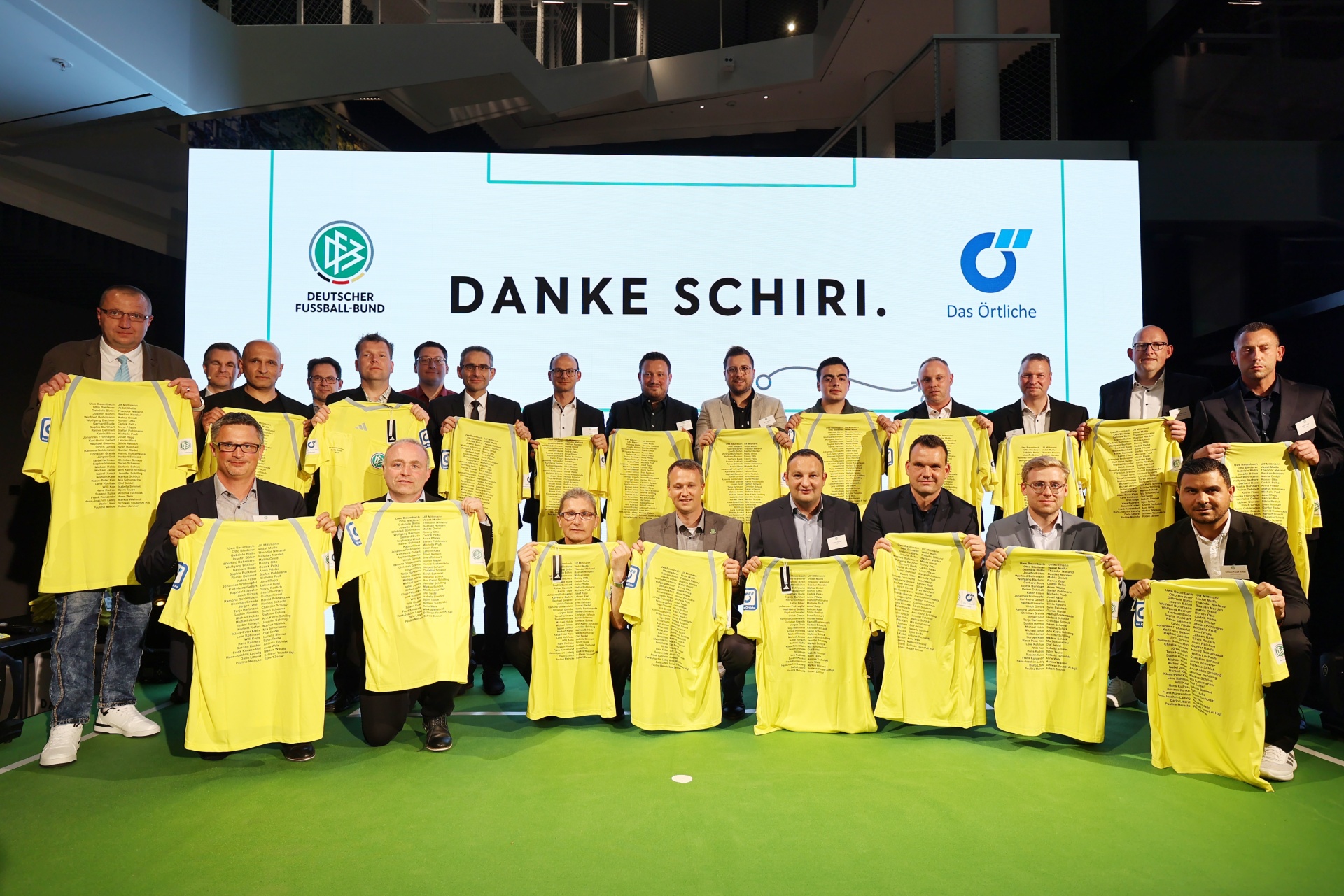 [{"clang_id":1,"value":"Gruppe von Männern mit gelben Fußballtrikots, vor einer Bühne mit dem Text \"DANKE SCHIRI.\" und Logos des Deutschen Fußball-Bundes und eines Sponsors."}]