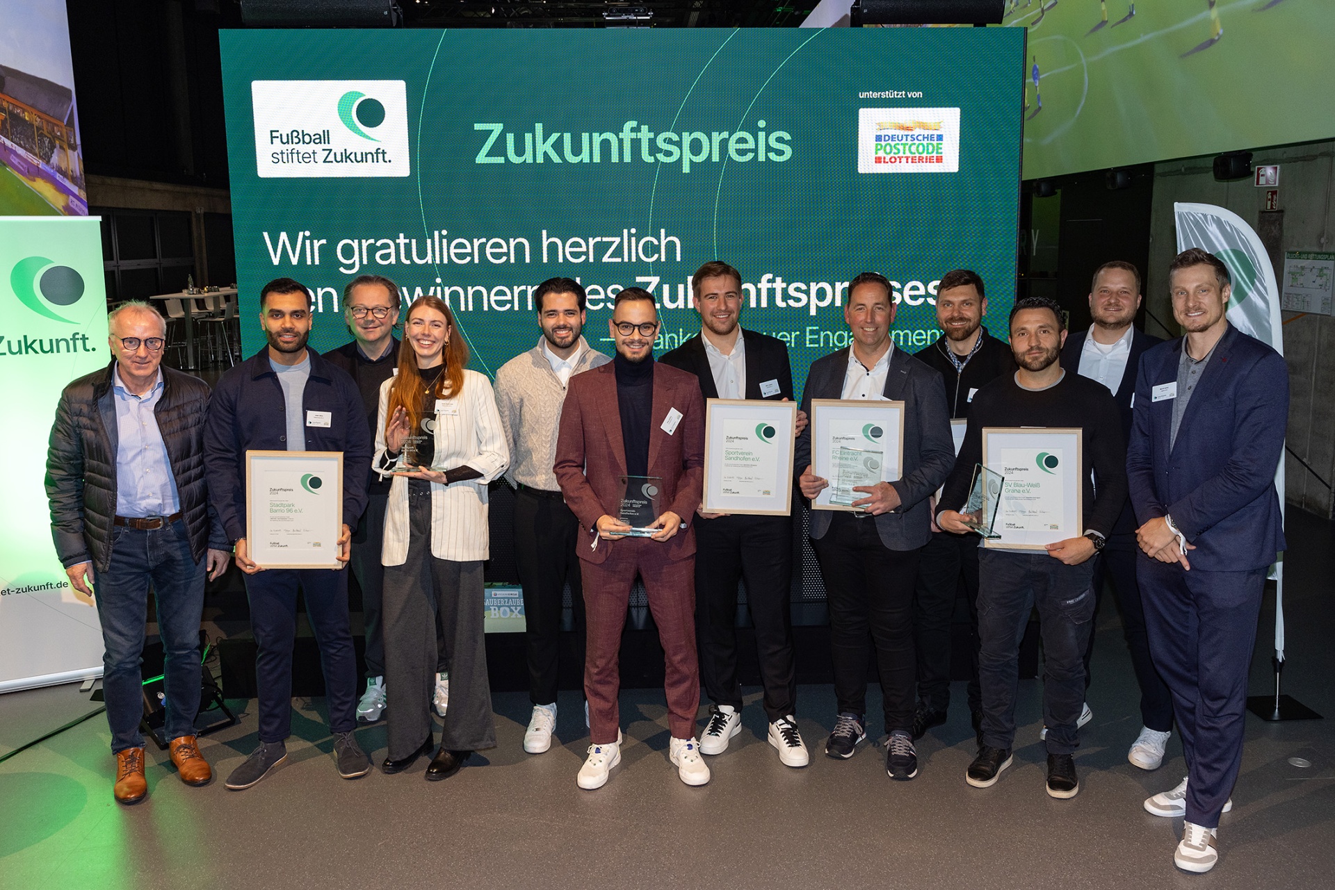 [{"clang_id":1,"value":"Gruppe von zehn Personen steht auf einer Bühne vor einem Banner mit dem Aufdruck \"Zukunftspreis\". Alle halten Auszeichnungen in den Händen."}]