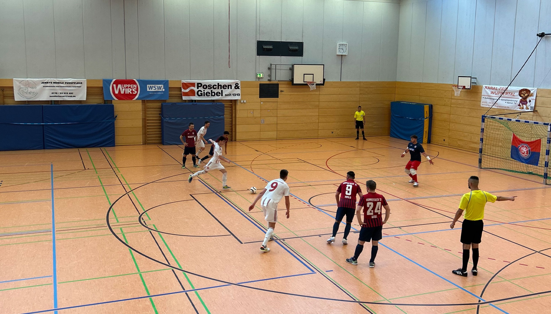[{"clang_id":1,"value":"Handballspiel in Sporthalle. Spieler in rot und weiß kämpfen um den Ball. Schiedsrichter in gelb. Banner an den Wänden."}]