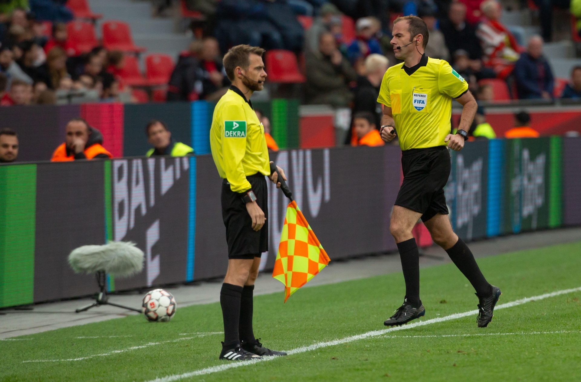 [{"clang_id":1,"value":"Zwei Fußballschiedsrichter in gelben Trikots und schwarzer Hose auf dem Spielfeld. Einer hält eine gelb-schwarze Fahne hoch, im Hintergrund Zuschauer."}]