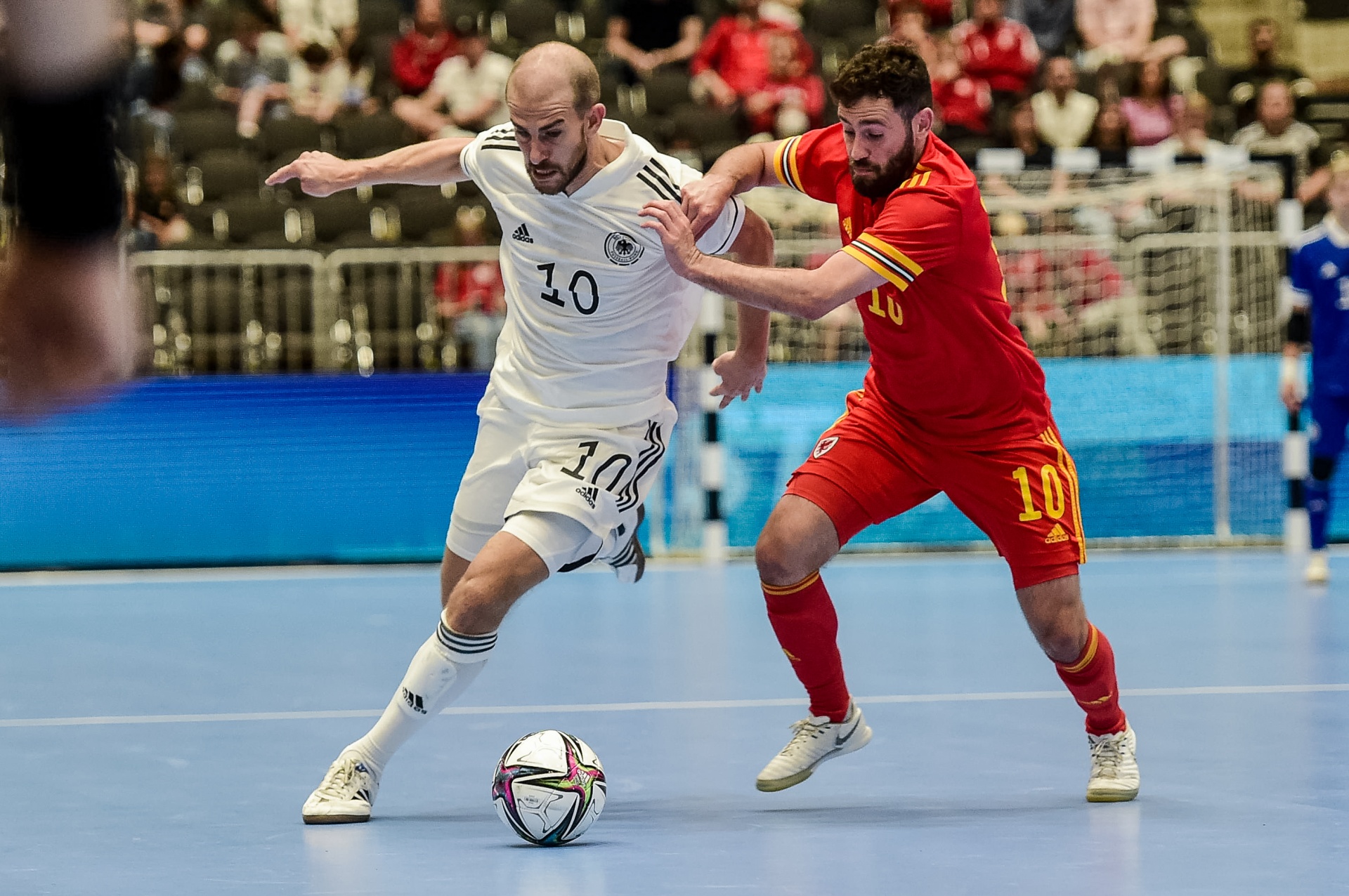 [{"clang_id":1,"value":"Futsal-Spiel: Spieler mit Nummer 10 (weißes Trikot, Deutschland) dribbelt den Ball, wird von Spieler mit Nummer 10 (rotes Trikot, Spanien) gedeckt. Stadion-Hintergrund."}]