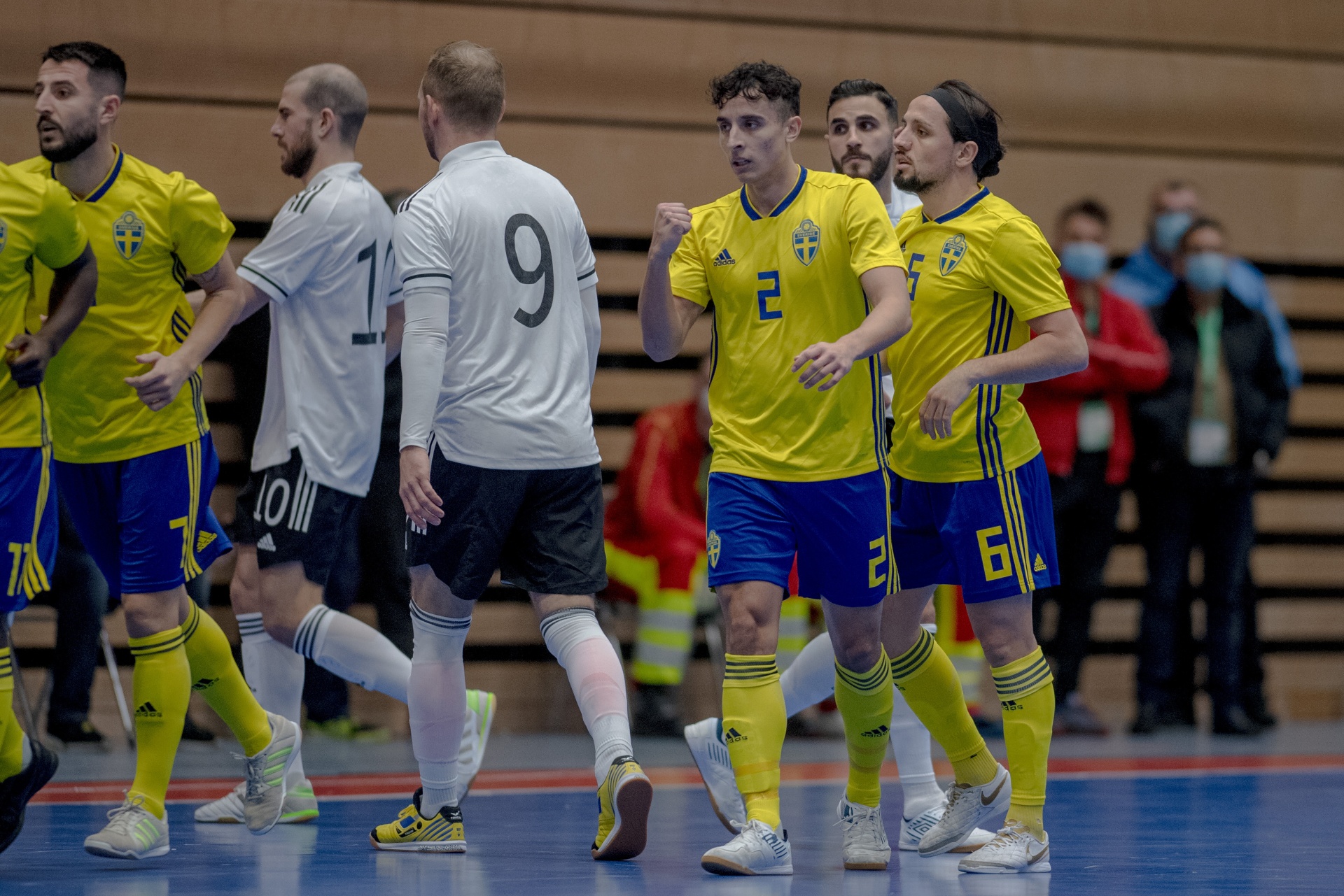 [{"clang_id":1,"value":"Futsalspieler in blau-gelben Trikots feiern. Zwei Spieler mit den Nummern 2 und 6 stehen im Vordergrund, andere Spieler und ein Schiedsrichter im Hintergrund. Indoor-Sportplatz."}]
