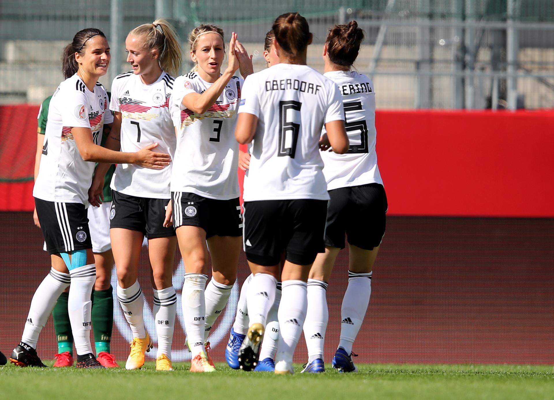 [{"clang_id":1,"value":"Fußballspielerinnen der deutschen Nationalmannschaft in schwarzen und weißen Trikots feiern gemeinsam auf dem Spielfeld. Im Hintergrund eine Zuschauertribüne."}]