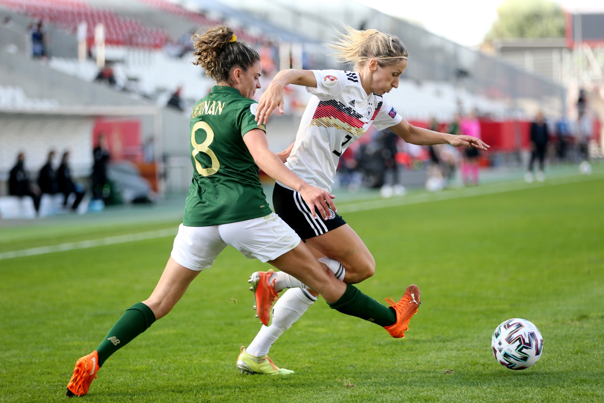 [{"clang_id":1,"value":"Zwei Fußballspielerinnen kämpfen um den Ball. Links trägt eine Spielerin ein grünes Trikot mit Nummer 8, rechts ein weiß-schwarzes Trikot. Rasen und Zuschauerränge im Hintergrund."}]