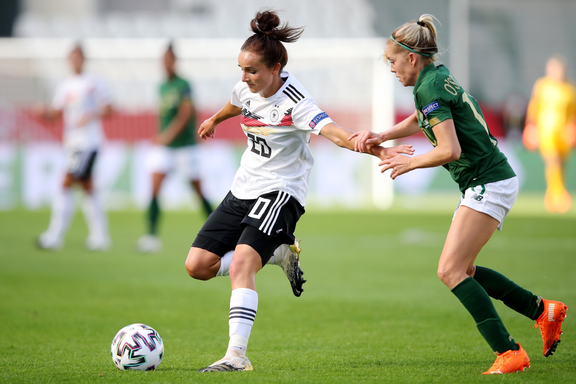 [{"clang_id":1,"value":"Fußballspiel: Spielerin mit Nummer 10 in Weiß dribbelt am Ball, wird von Gegenspielerin in Grün und Weiß gedeckt. Rasenplatz im Hintergrund."}]
