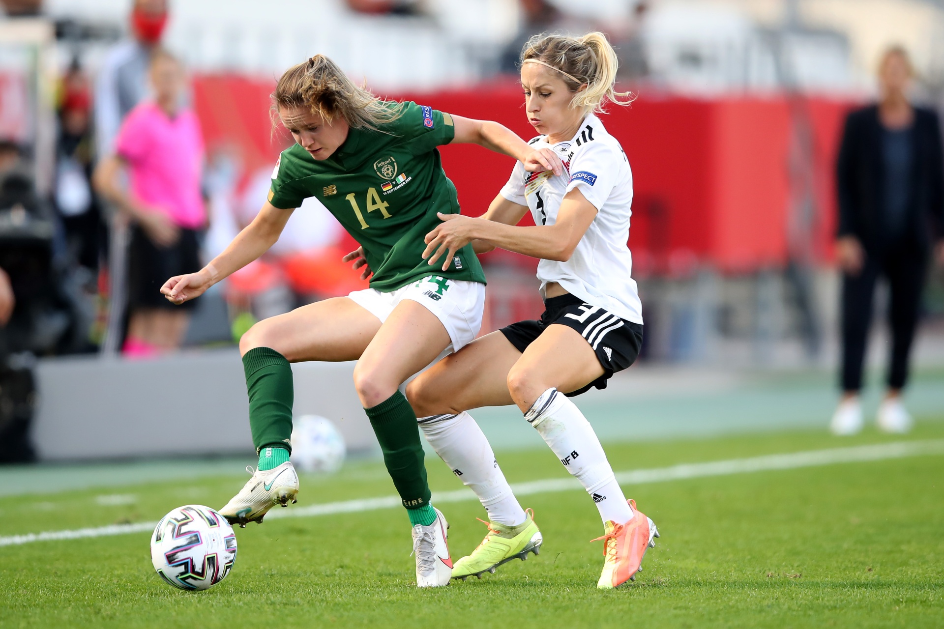[{"clang_id":1,"value":"Zwei Fußballspielerinnen kämpfen um den Ball auf grünem Rasen. Links trägt eine Spielerin ein grünes Trikot mit der Nummer 14, rechts ein weiß-schwarzes Trikot."}]