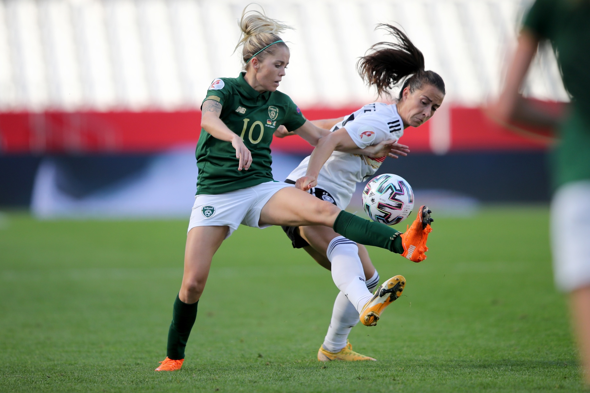 [{"clang_id":1,"value":"Zwei Fußballspielerinnen kämpfen um den Ball. Links in grünem Trikot mit Nummer 10, rechts in weiß-rotem Trikot. Rasen im Hintergrund."}]
