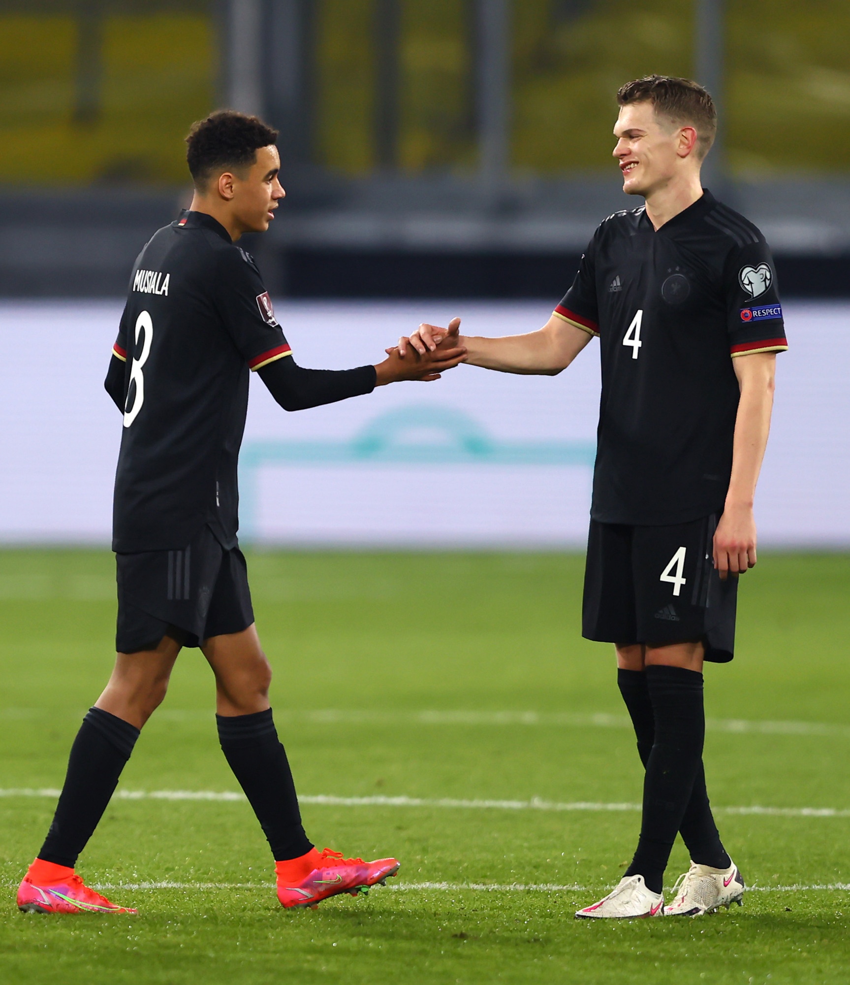[{"clang_id":1,"value":"Zwei Fußballspieler in schwarzen Trikots mit roten Akzenten stehen auf dem Spielfeld und geben sich die Hände. Spieler links trägt die Nummer 8, rechts die 4."}]