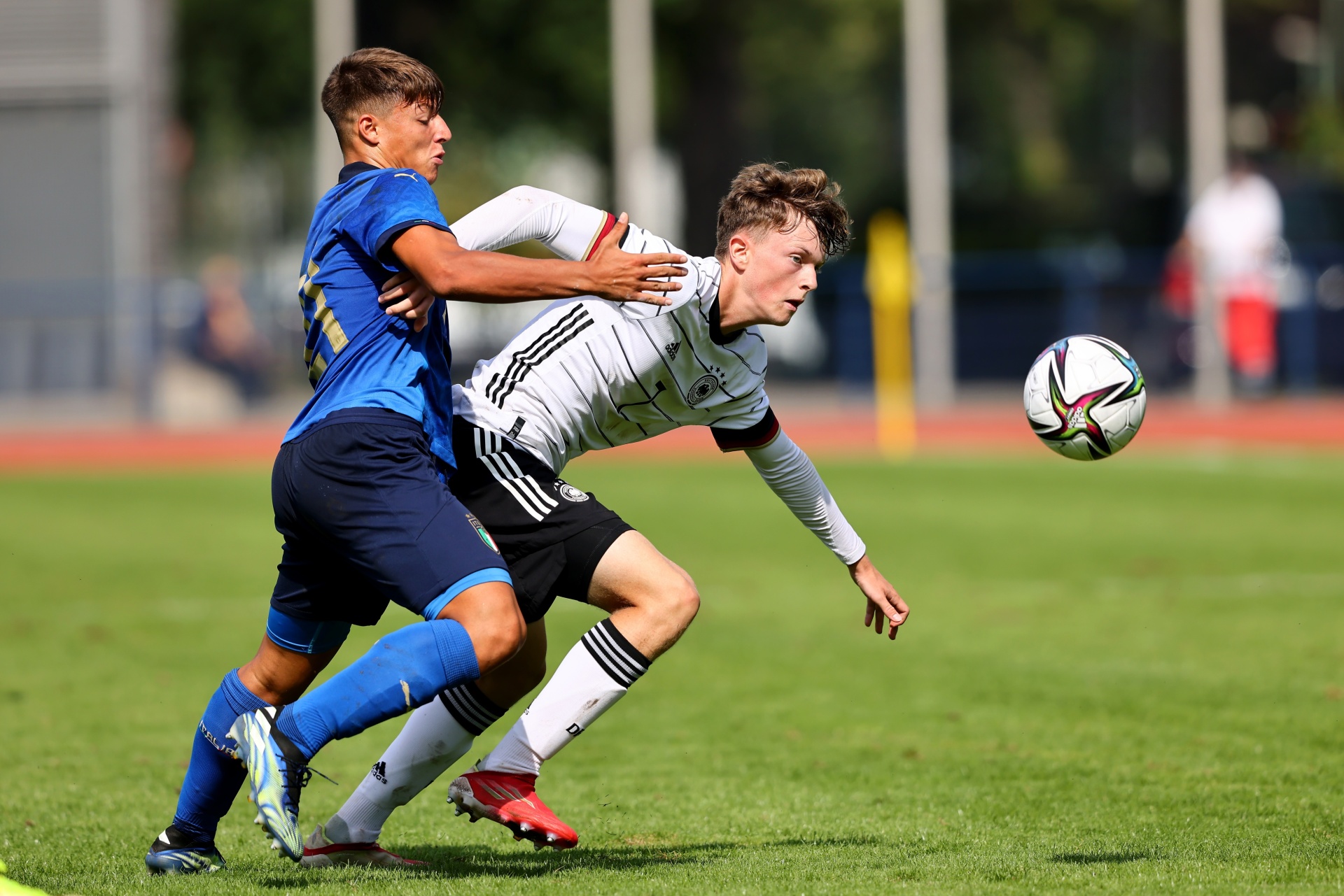 [{"clang_id":1,"value":"Zwei Fußballspieler im Zweikampf auf grünem Rasen. Links Spieler mit blauem Trikot, rechts Spieler mit schwarz-weiß gestreiftem Trikot. Im Hintergrund Zuschauer und ein Fußball."}]