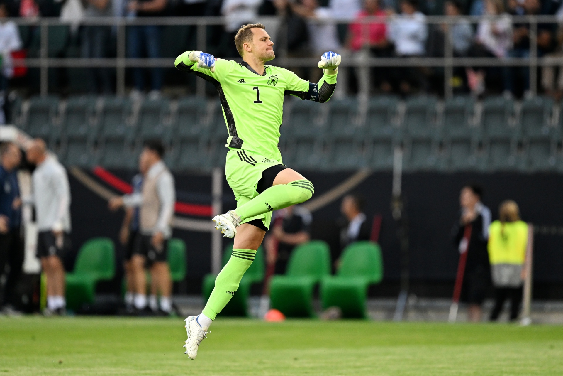 [{"clang_id":1,"value":"Fußballtorwart springt jubelnd in die Luft. Er trägt grüne Torwartkleidung mit Nummer 1. Im Hintergrund Zuschauerreihen und grüne Sitzbänke."}]
