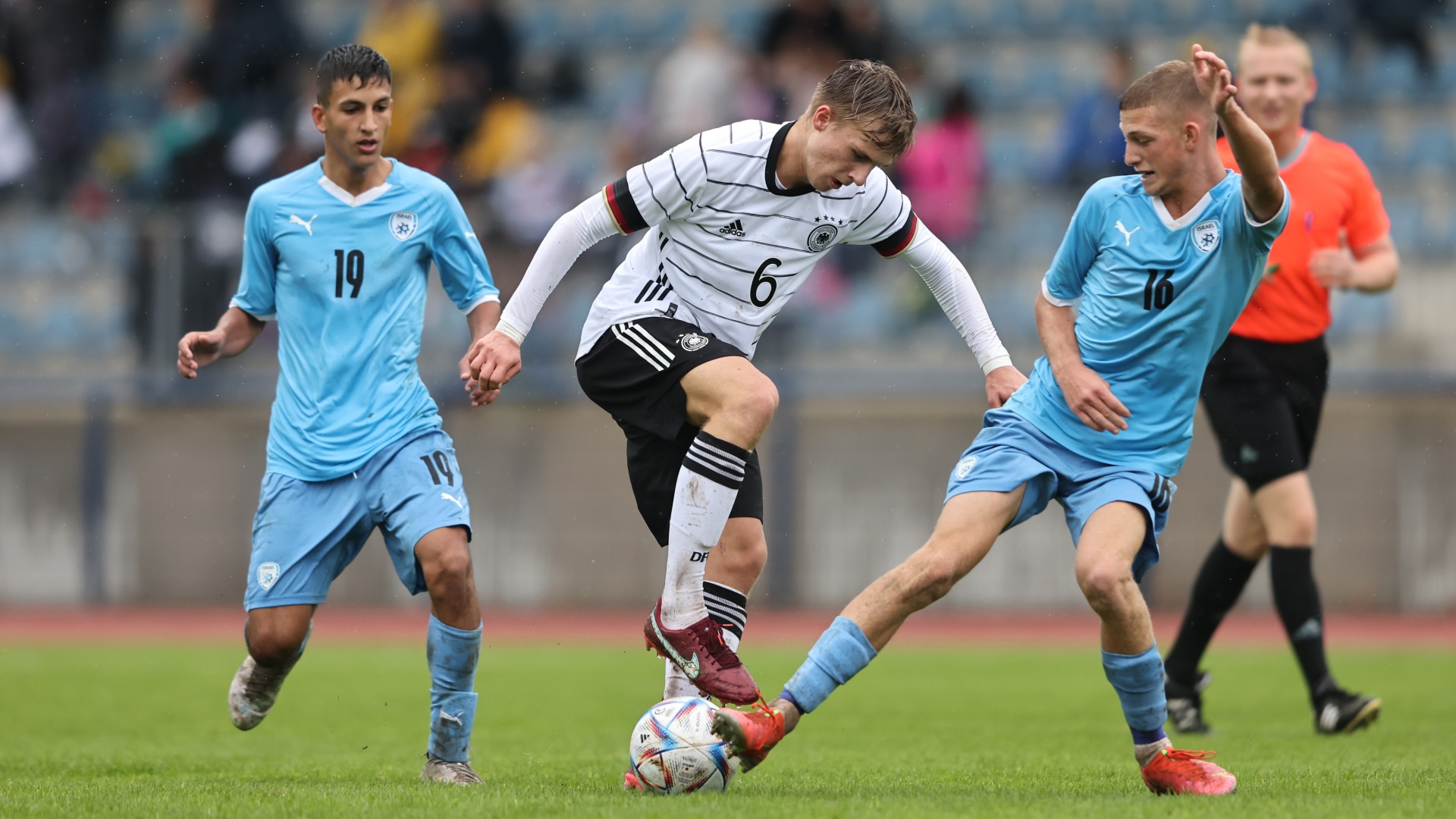 [{"clang_id":1,"value":"Fußballspiel: Spieler mit Nummer 6 in Deutschlandtrikot dribbelt den Ball, wird von zwei Spielern in blauem Trikot angegriffen. Grünrasen im Hintergrund."}]