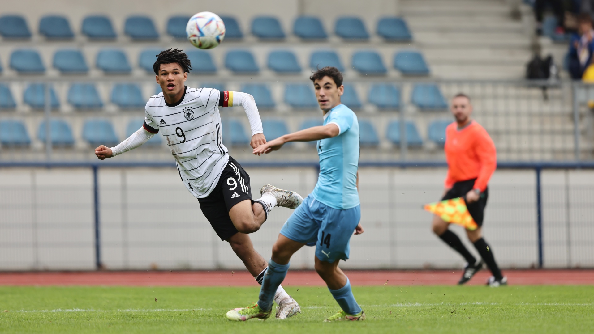 [{"clang_id":1,"value":"Zwei Fußballspieler im Spiel: Spieler mit Nummer 9 in Schwarz-Weiß versucht Ball zu köpfen, wird von Spieler mit Nummer 14 in Hellblau gefoult. Stadion im Hintergrund."}]