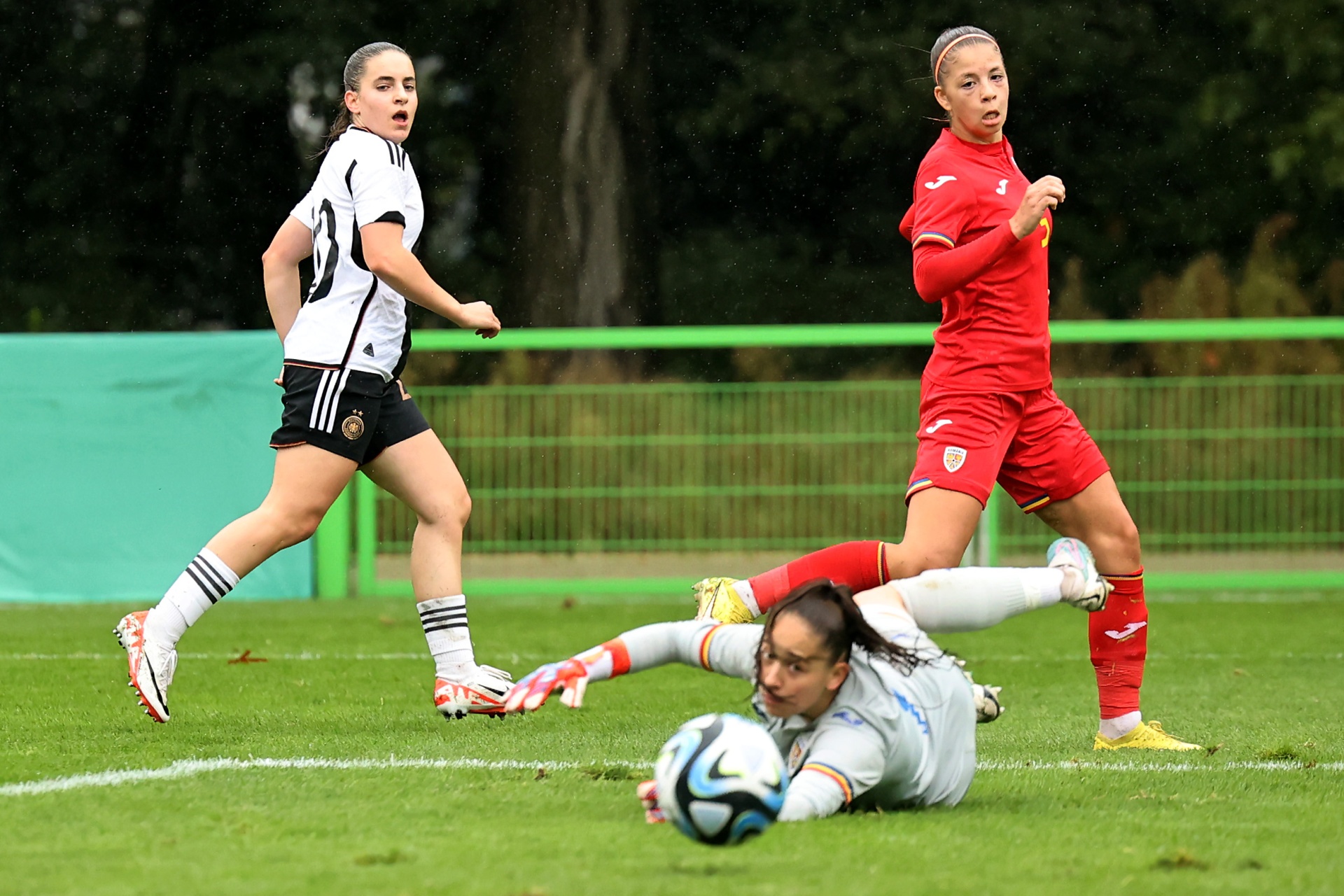 [{"clang_id":1,"value":"Fußballspiel: Spielerin in Schwarz wird von Spielerin in Rot gefoult, während Torwartin versucht, Ball zu halten. Rasenplatz im Hintergrund."}]